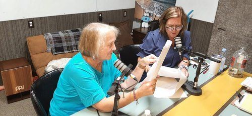 Two women are sitting at a table in front of microphones.