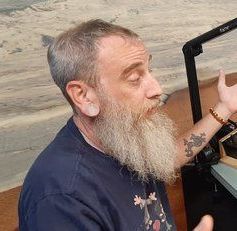 A man with a beard is sitting in front of a microphone.