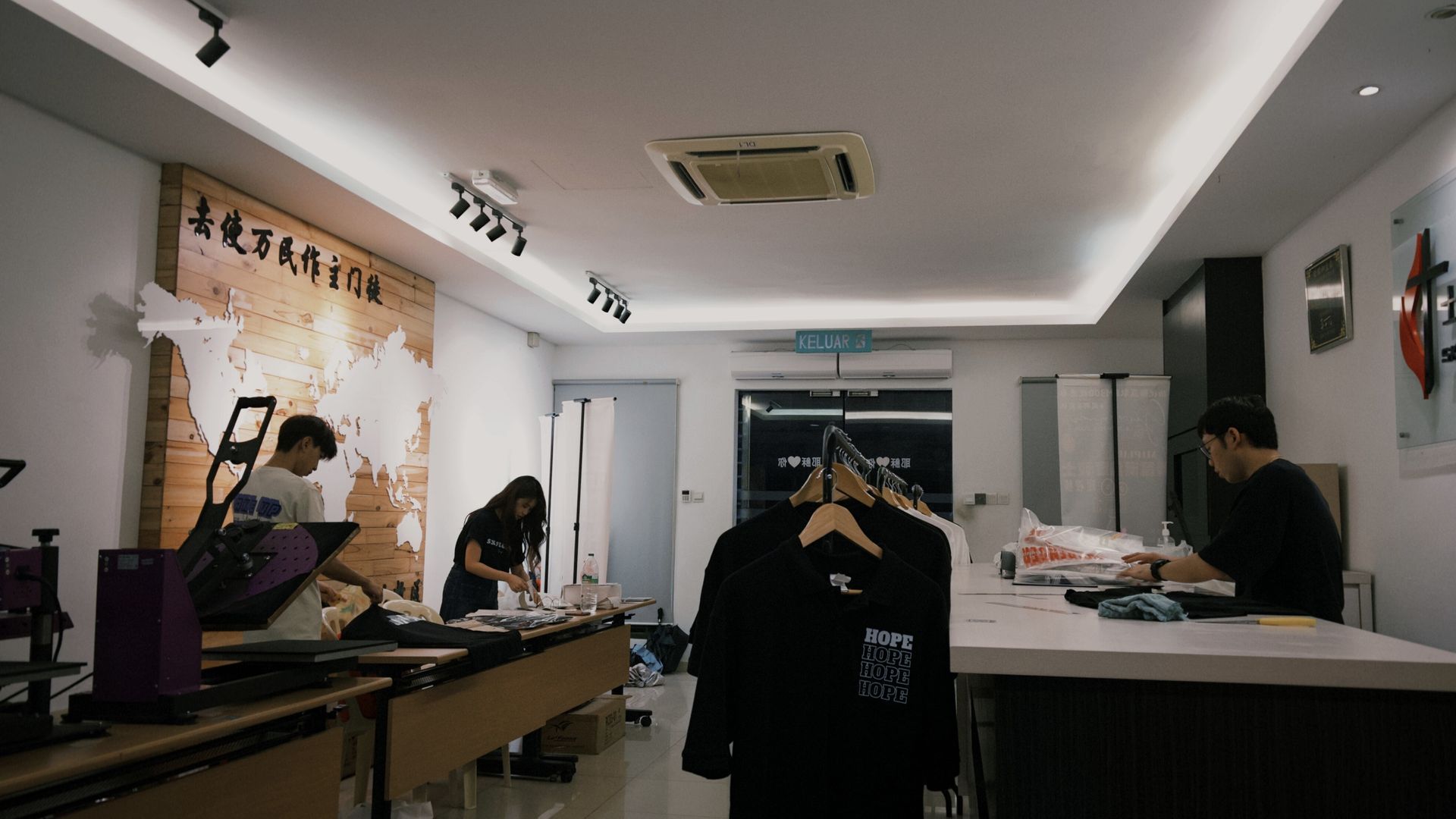 People working in a brightly lit clothing store, with a map on the wall and merchandise on display.