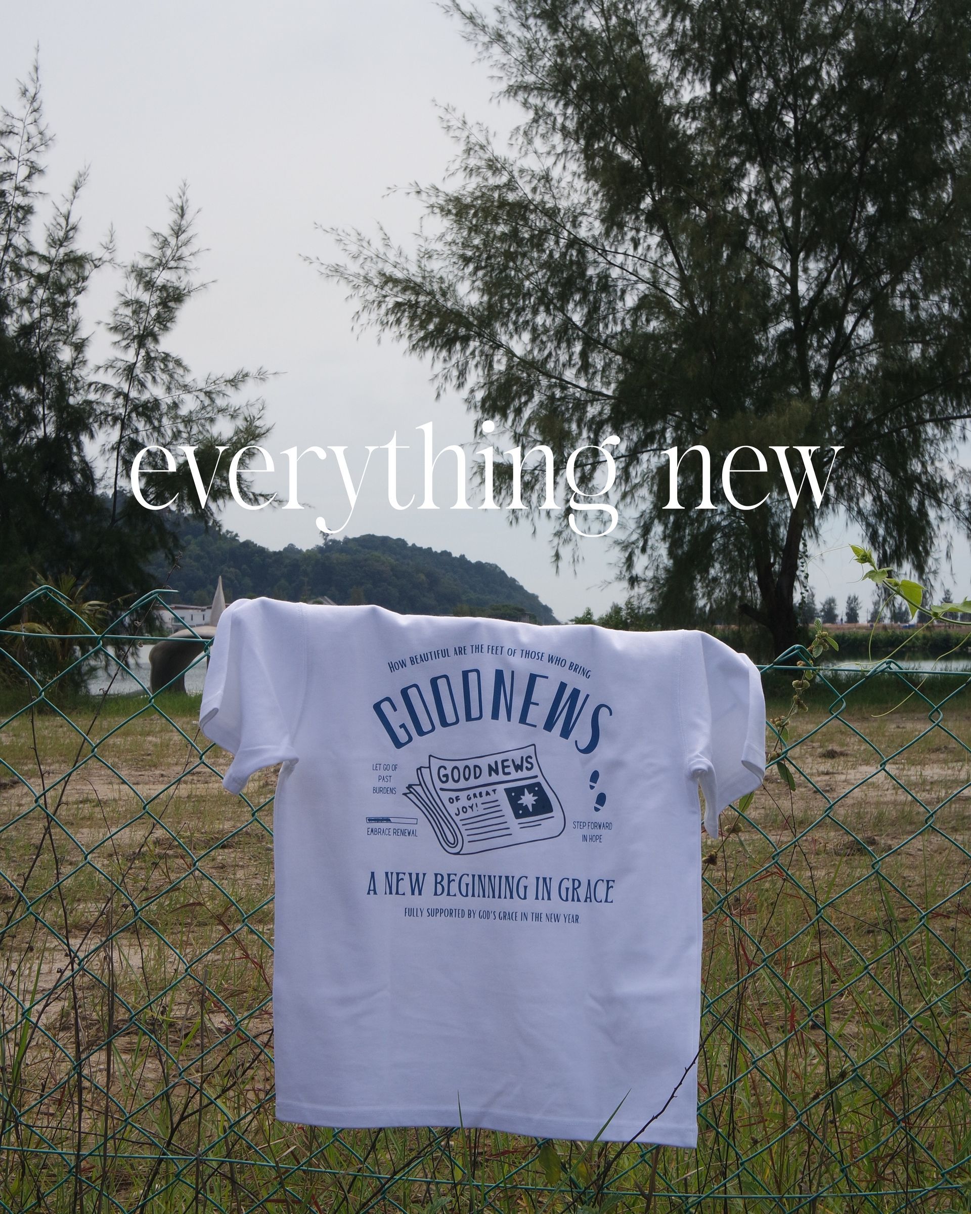 White t-shirt with blue graphic, hung on a fence in front of a landscape with text