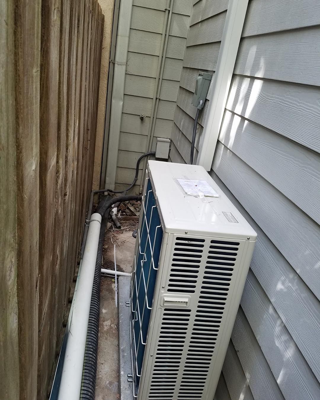 Air conditioning unit mounted next to a wooden fence and siding.