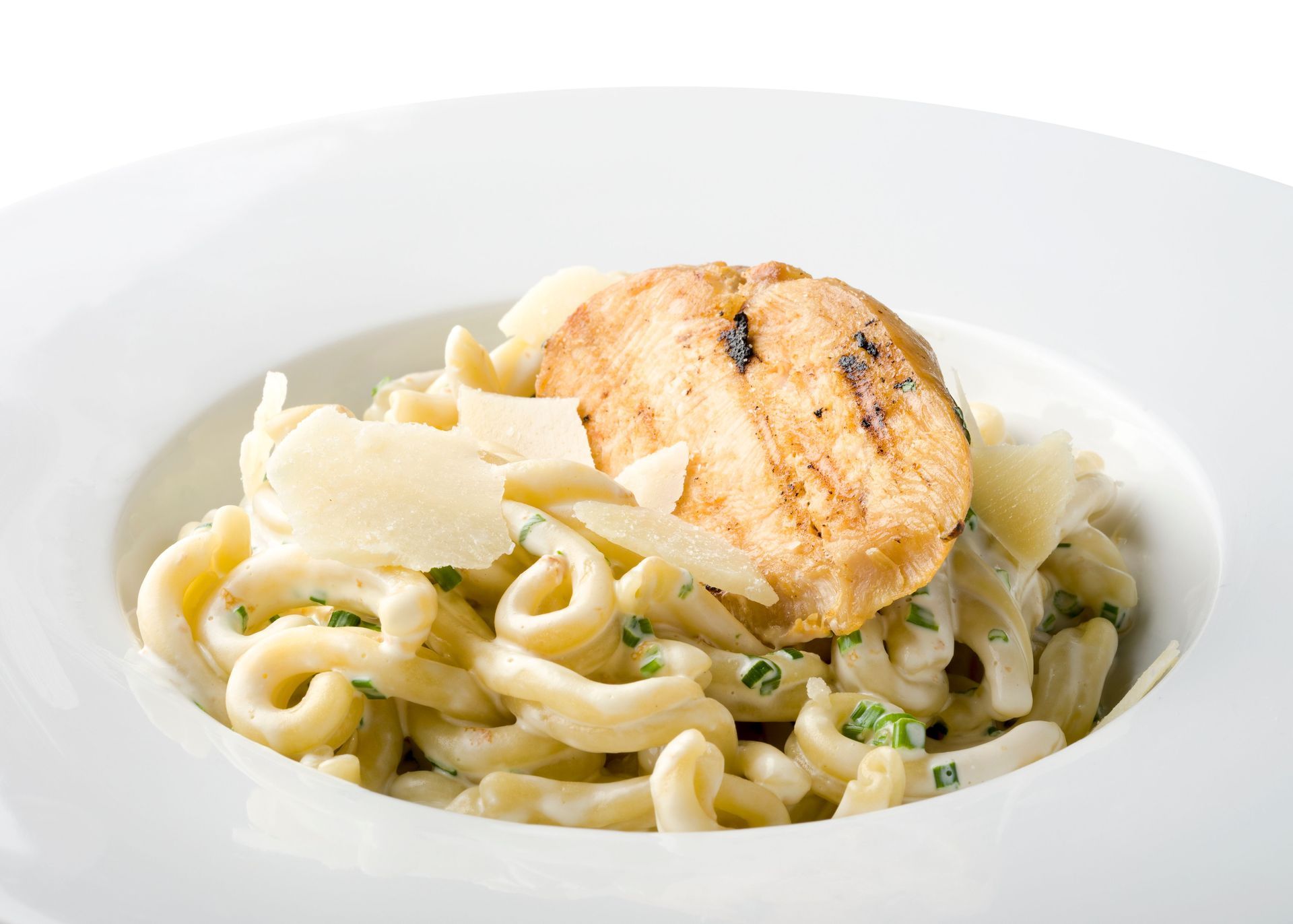 Creamy pasta with grilled chicken and shaved cheese in a white bowl