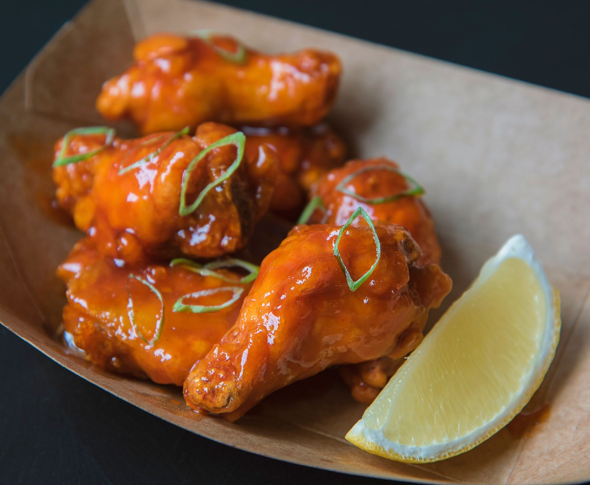 Glazed chicken wings on a paper tray with lemon wedge and green garnish