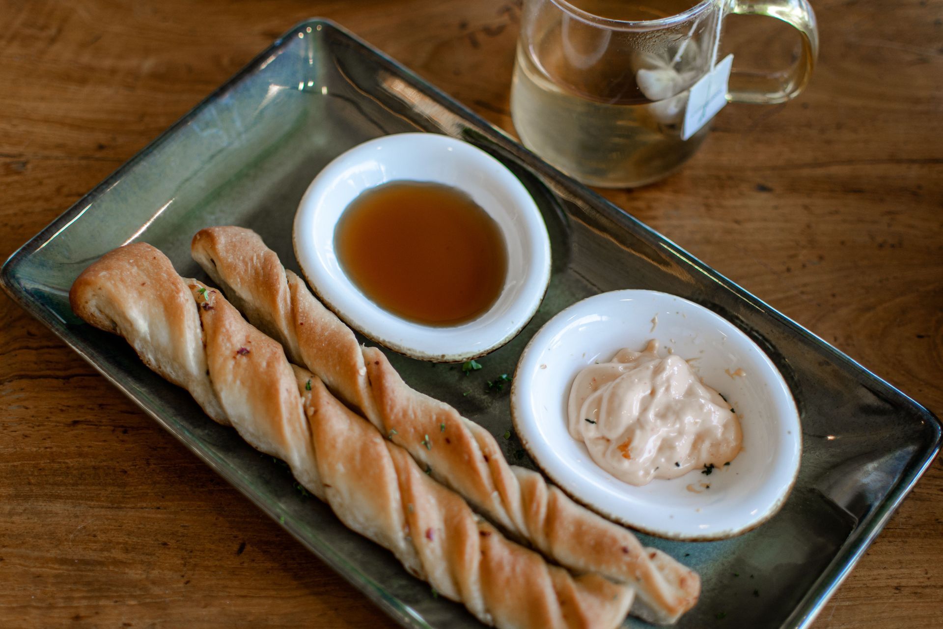 Breadsticks on a rectangular plate with dipping sauce and a small ramekin on a wooden table