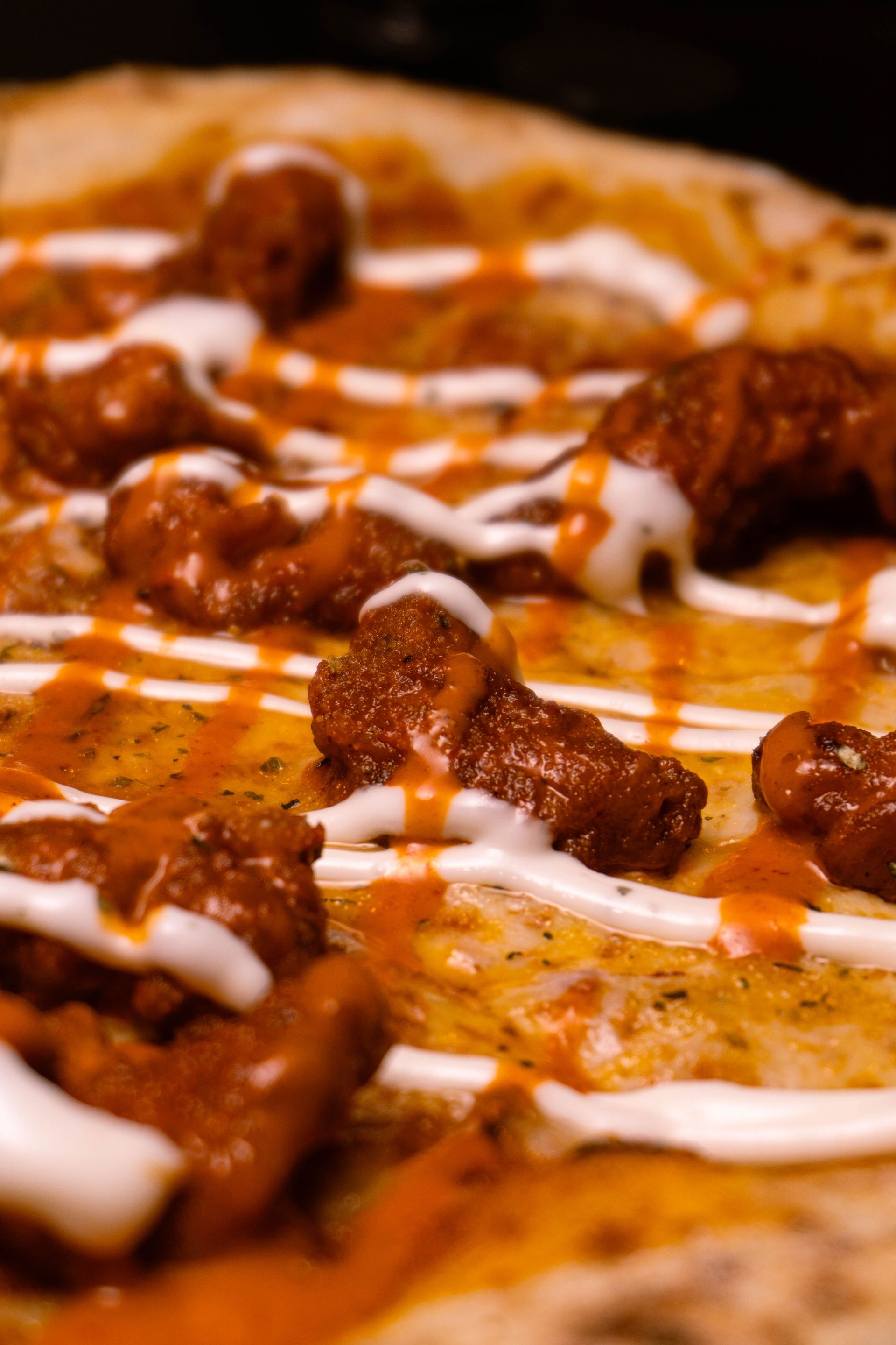 Close-up of a cheesy pizza topped with meat and drizzled with white sauce