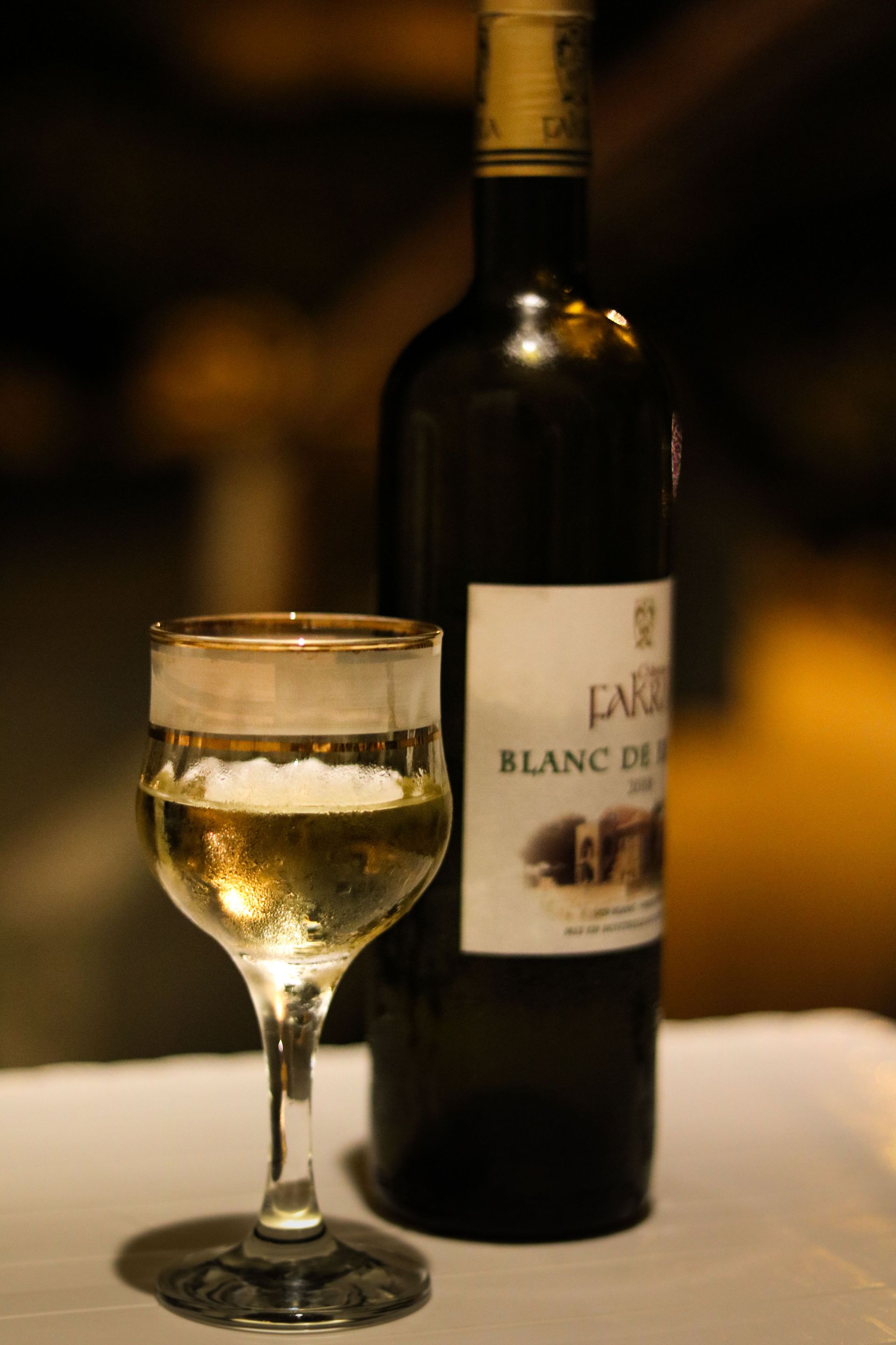 Wine glass and bottle of white wine on a table against a dark background