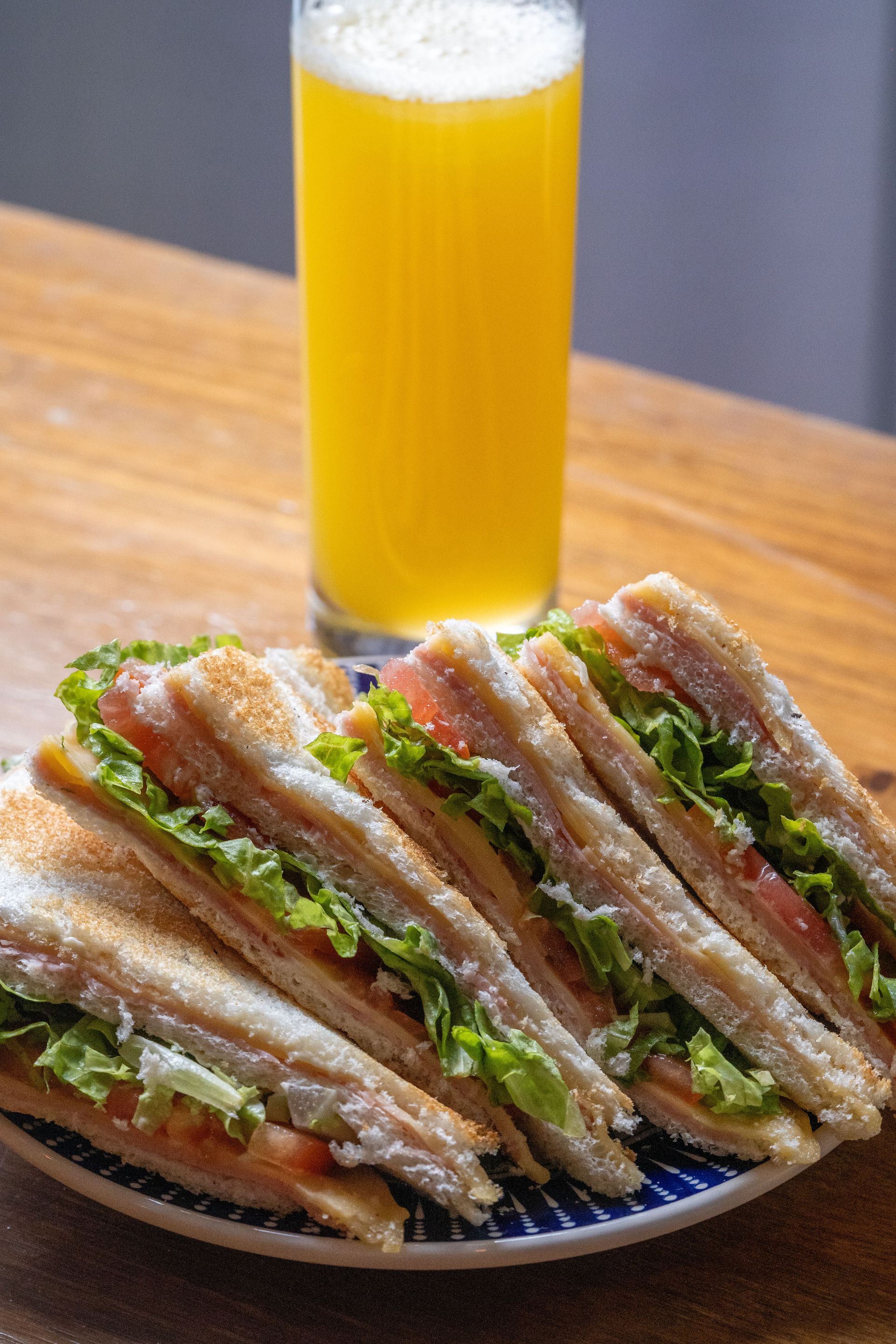 Stack of toasted sandwiches on a plate beside a tall glass of orange juice on a wooden table