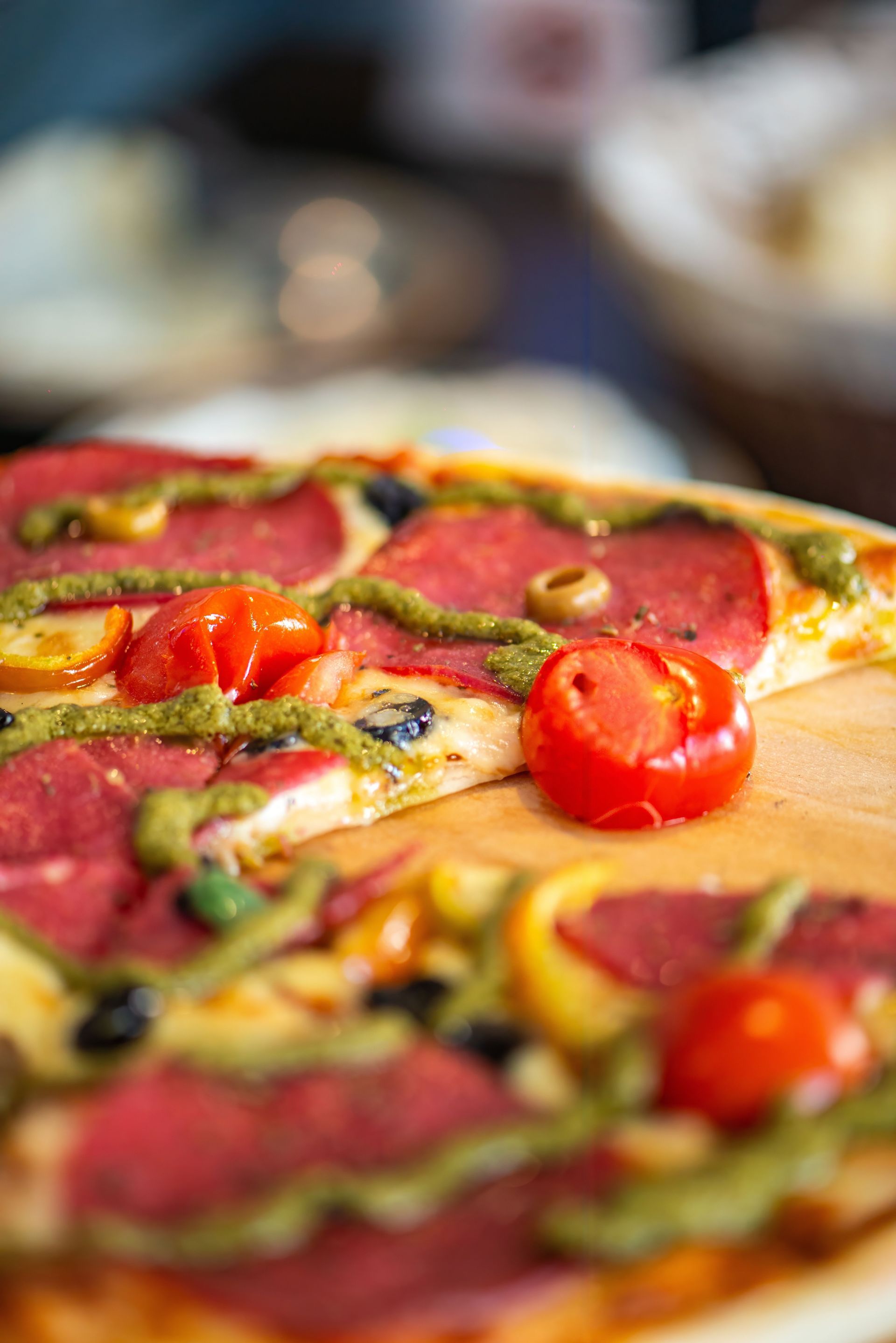 Close-up of a vegetable pizza with cherry tomatoes, green peppers, and olives on a wooden table