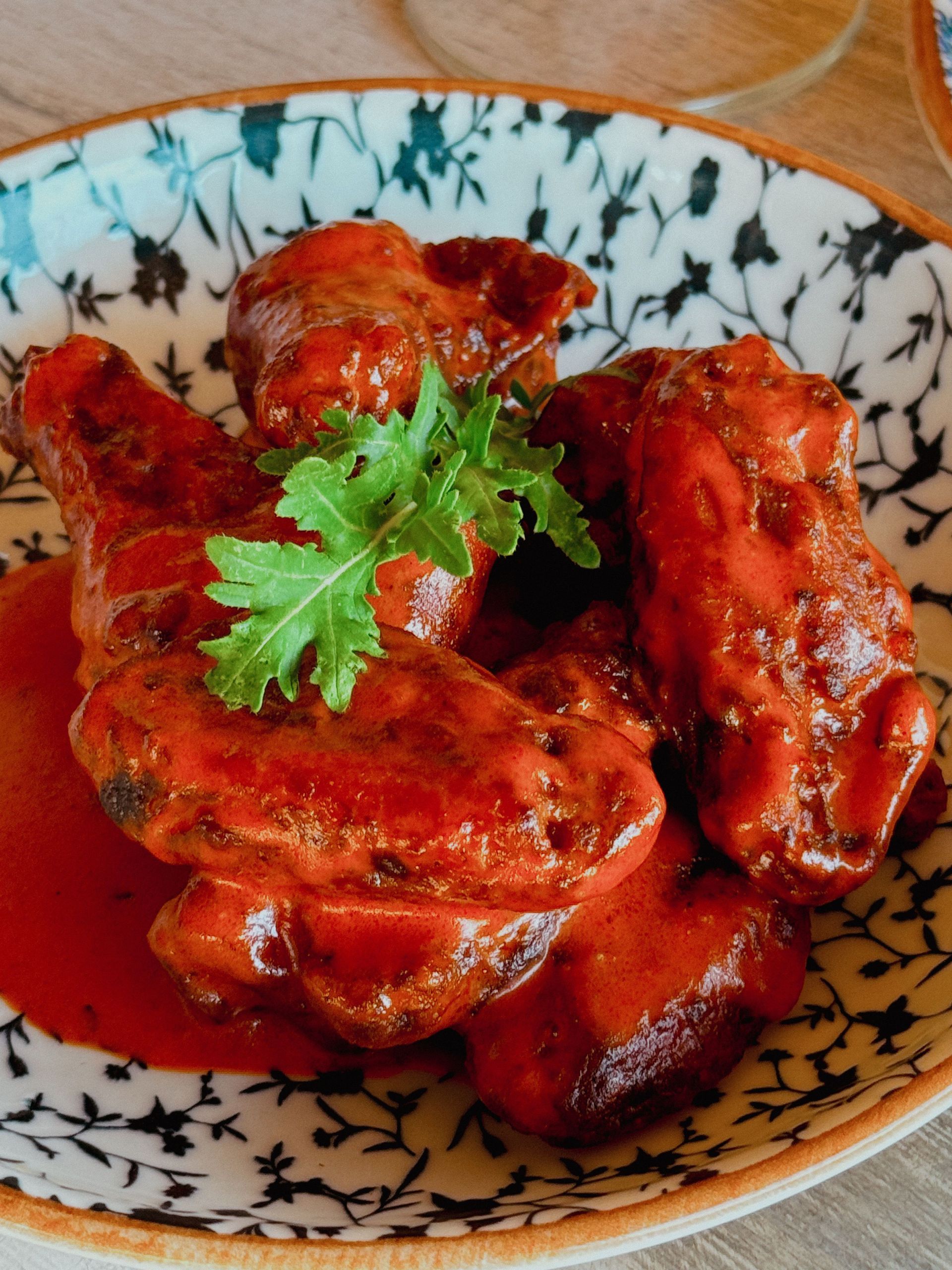Spicy glazed chicken wings in a patterned bowl, garnished with cilantro.