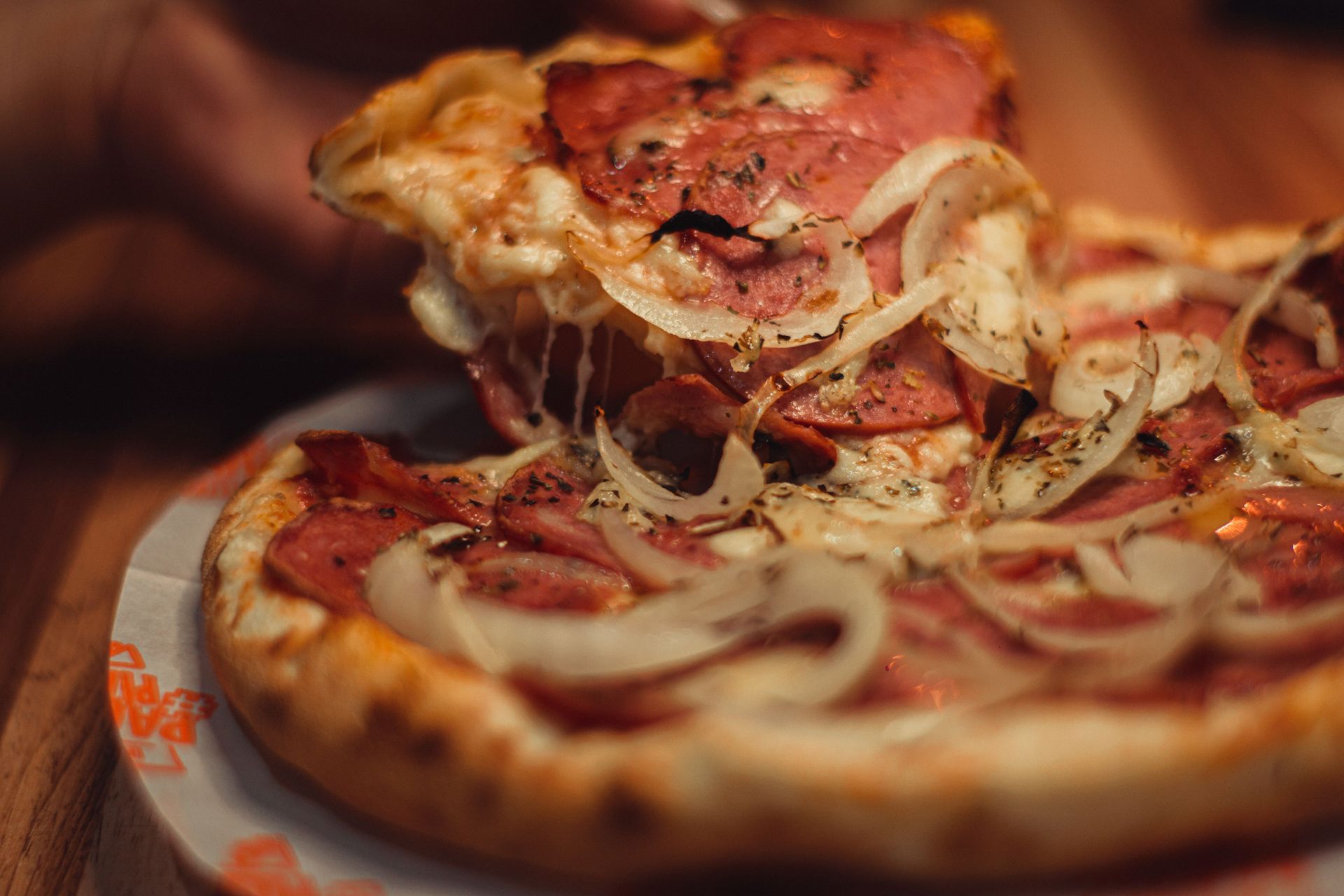 Close-up of a pepperoni pizza with onion slices and a hand lifting a slice