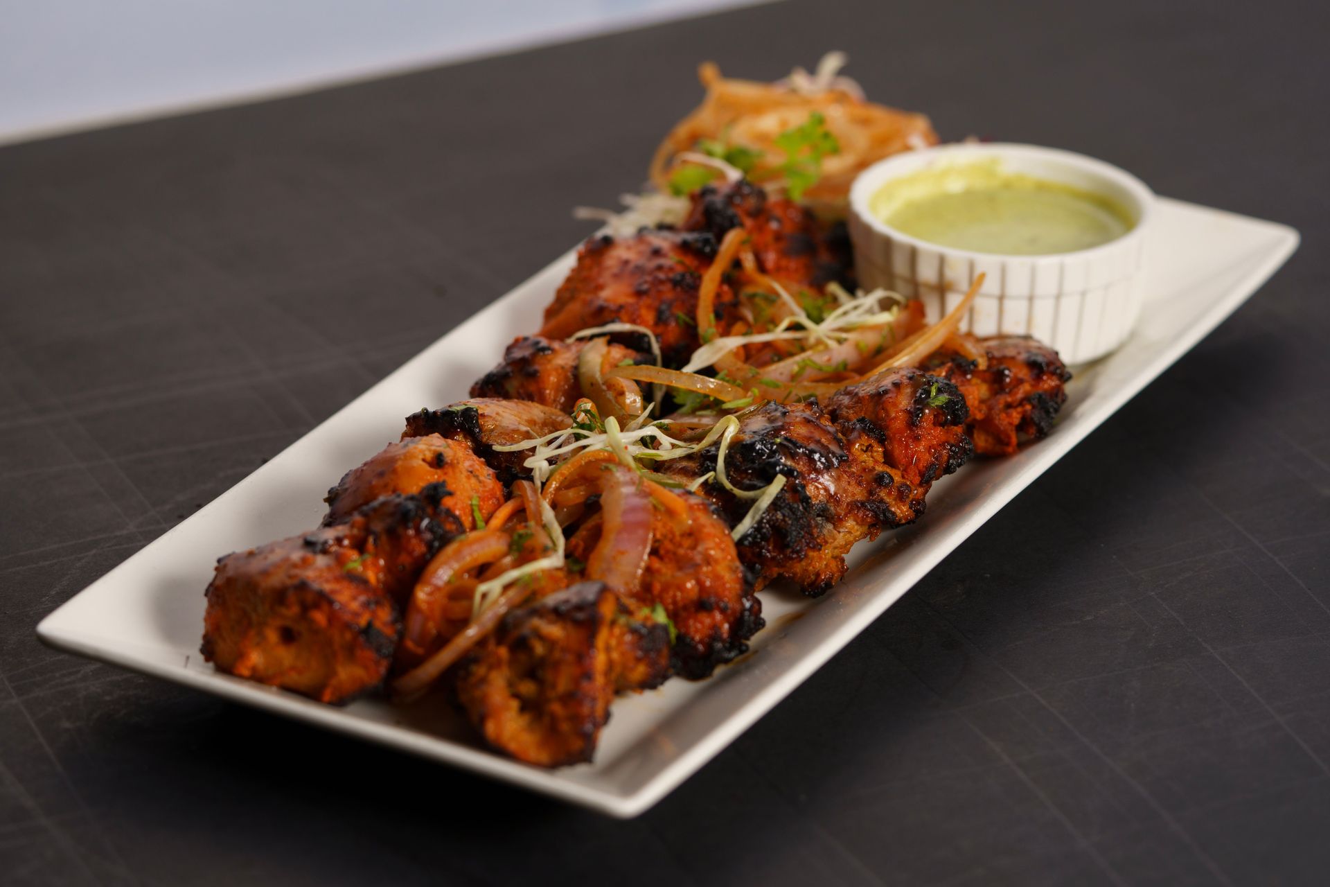 Grilled chicken skewers on a white platter with garnish and dipping sauce