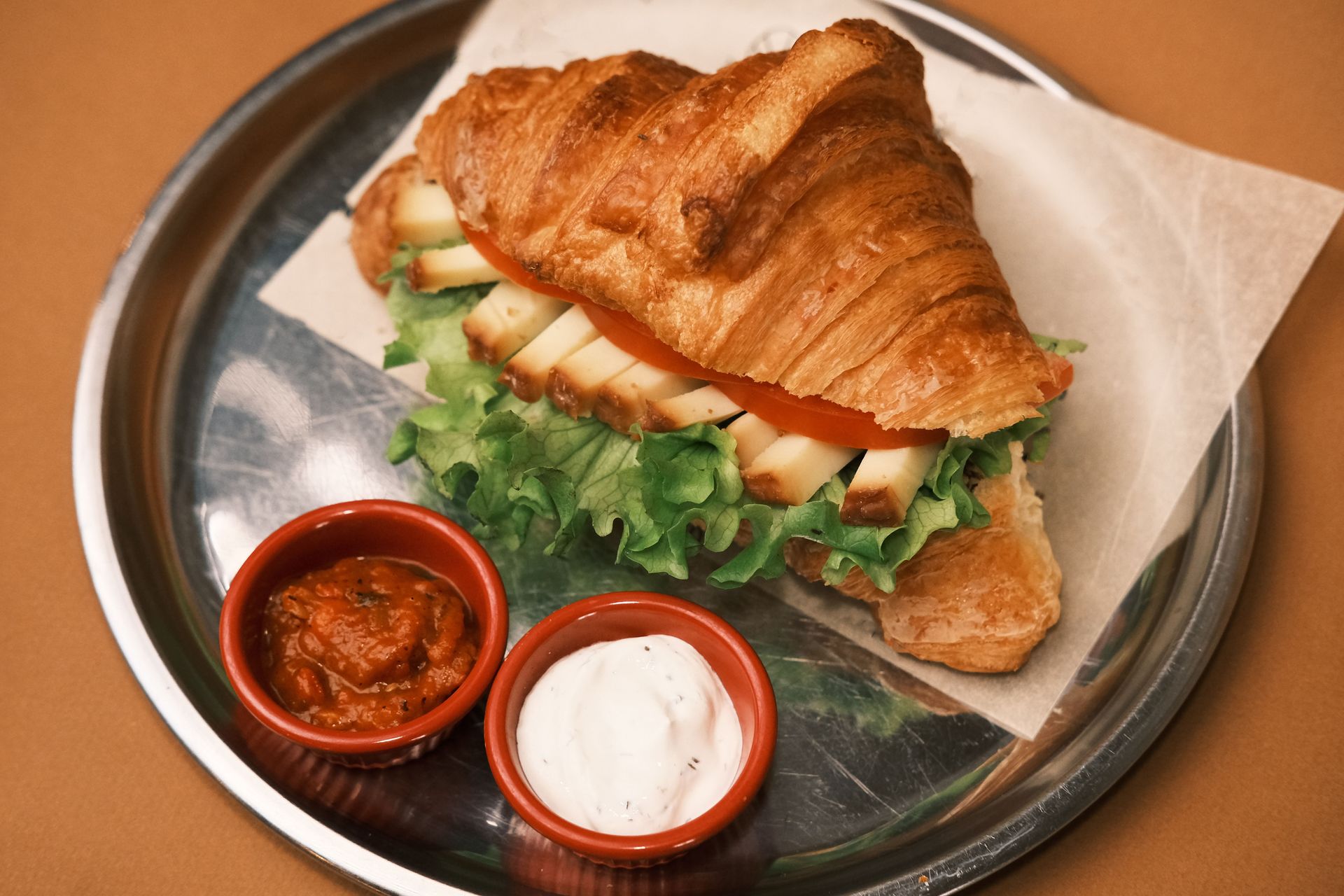 Croissant sandwich on a plate with two small dipping sauces