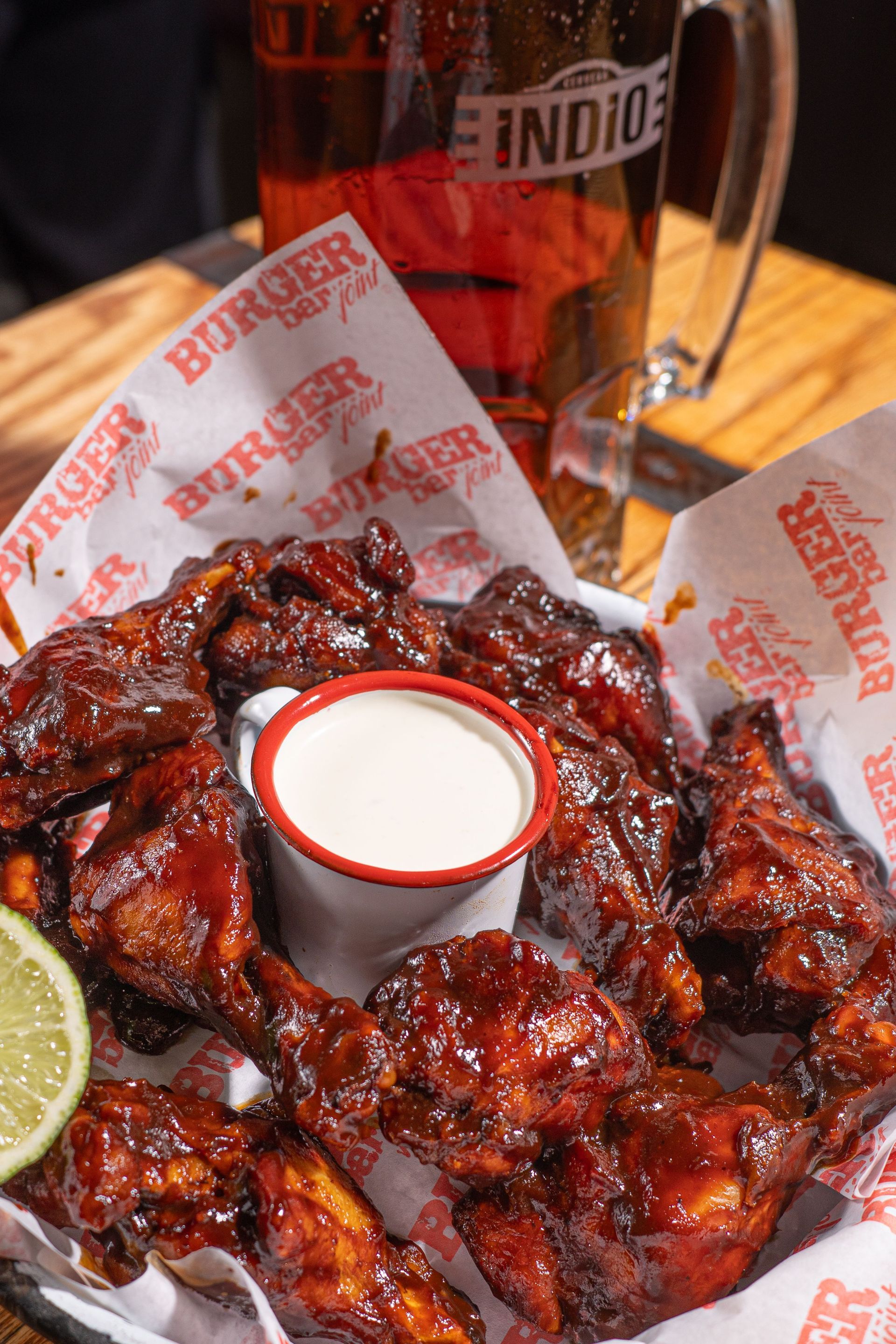 Saucy chicken wings with dipping sauce and lime on a tray, with a beer mug in the background
