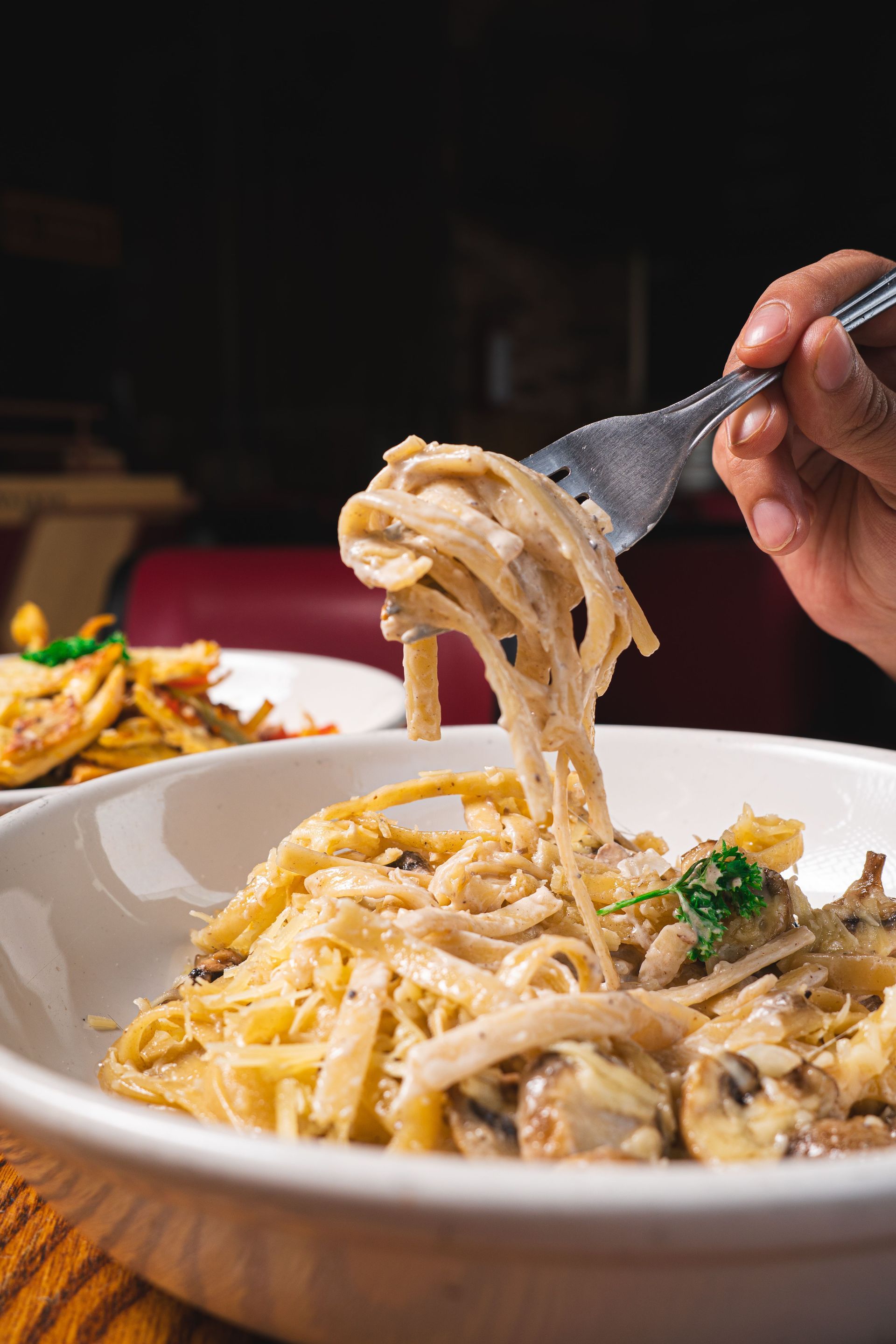 Hand lifting creamy pasta from a white bowl on a dining table
