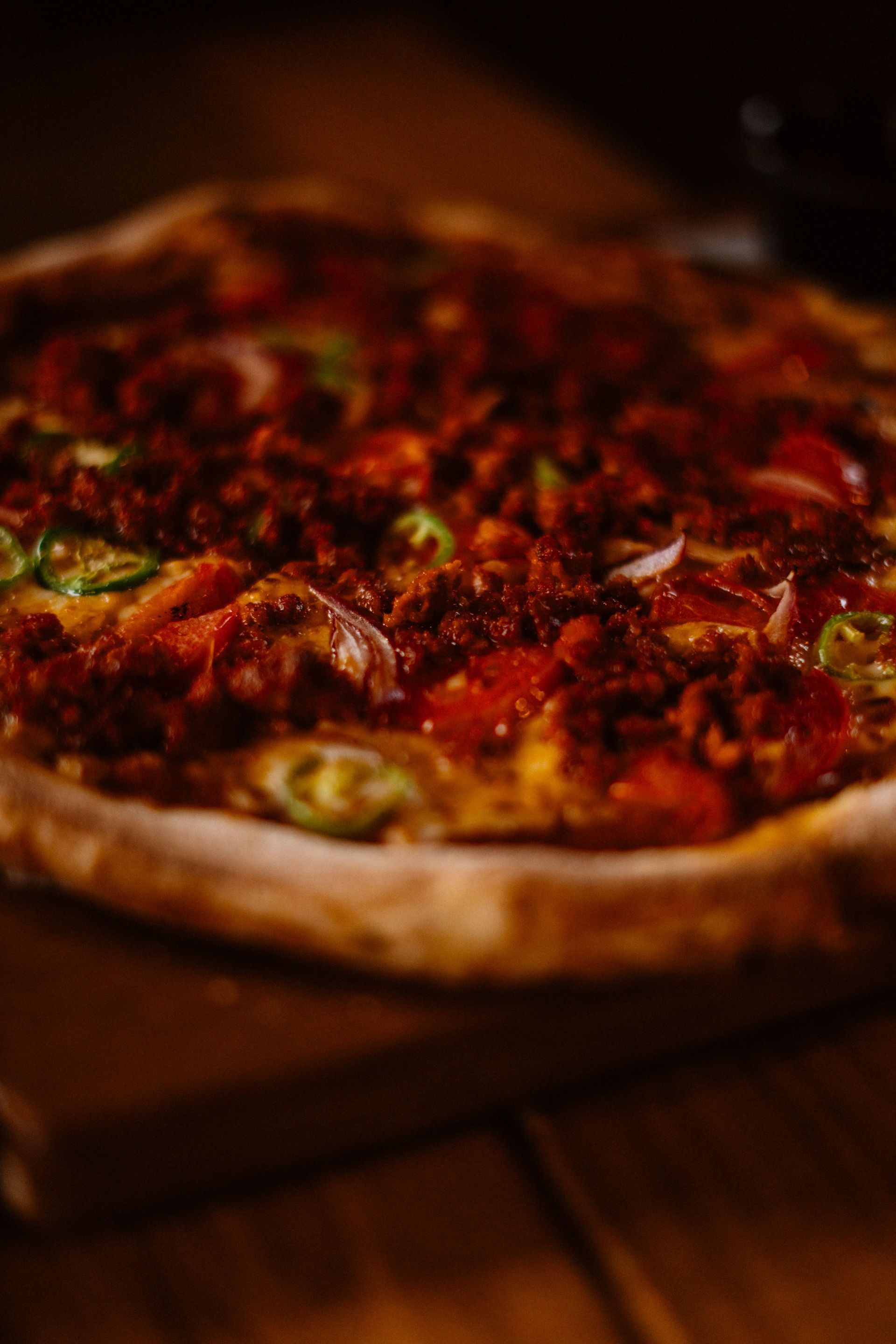 A close-up of a crispy pizza topped with red sauce and herbs on a wooden table.