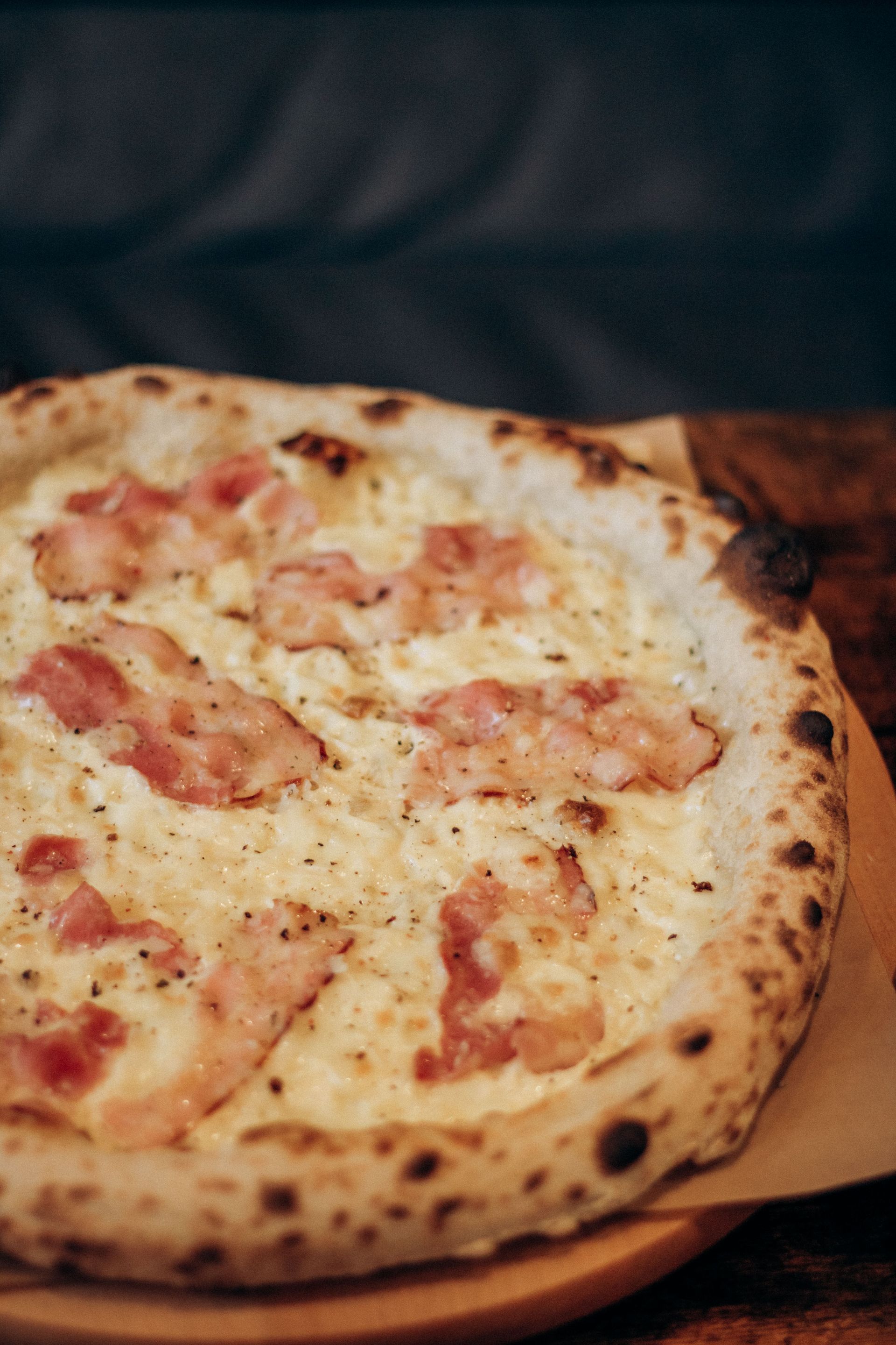 Wood-fired pizza with melted cheese and tomato slices on a wooden board