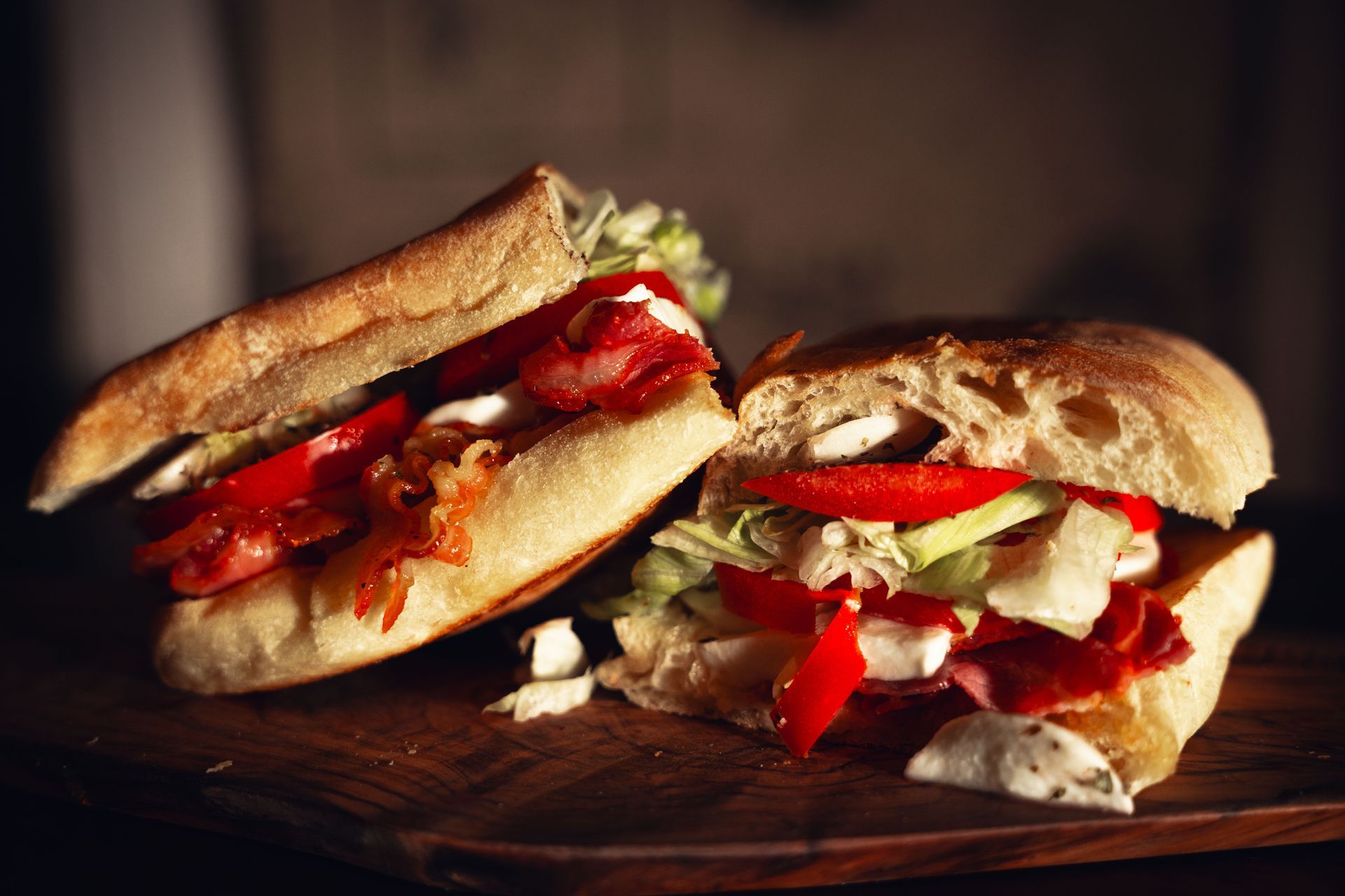 Two sandwiches with lettuce and red peppers on a wooden board