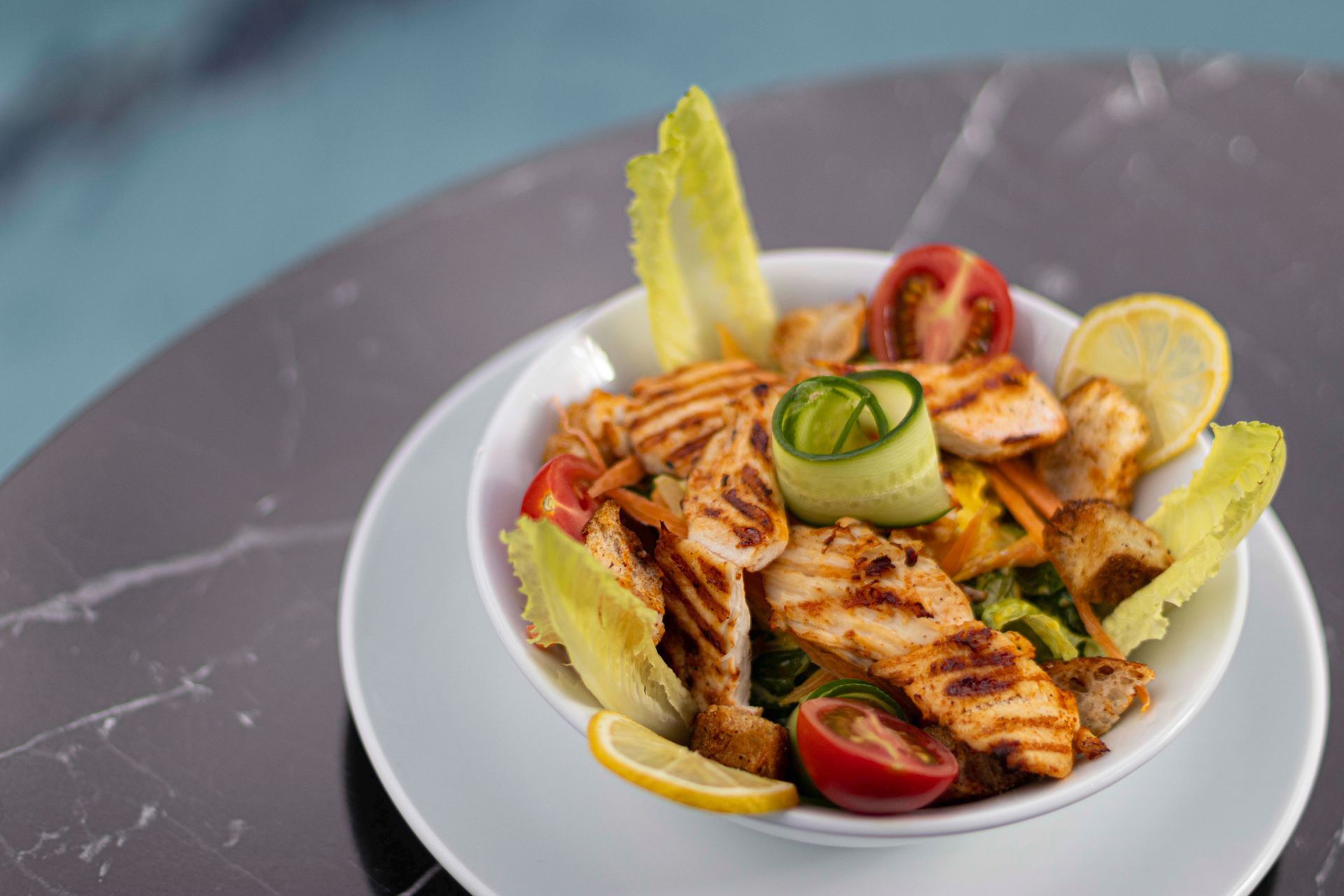 Grilled chicken salad with cucumber, tomatoes, and lemon wedges on a white plate