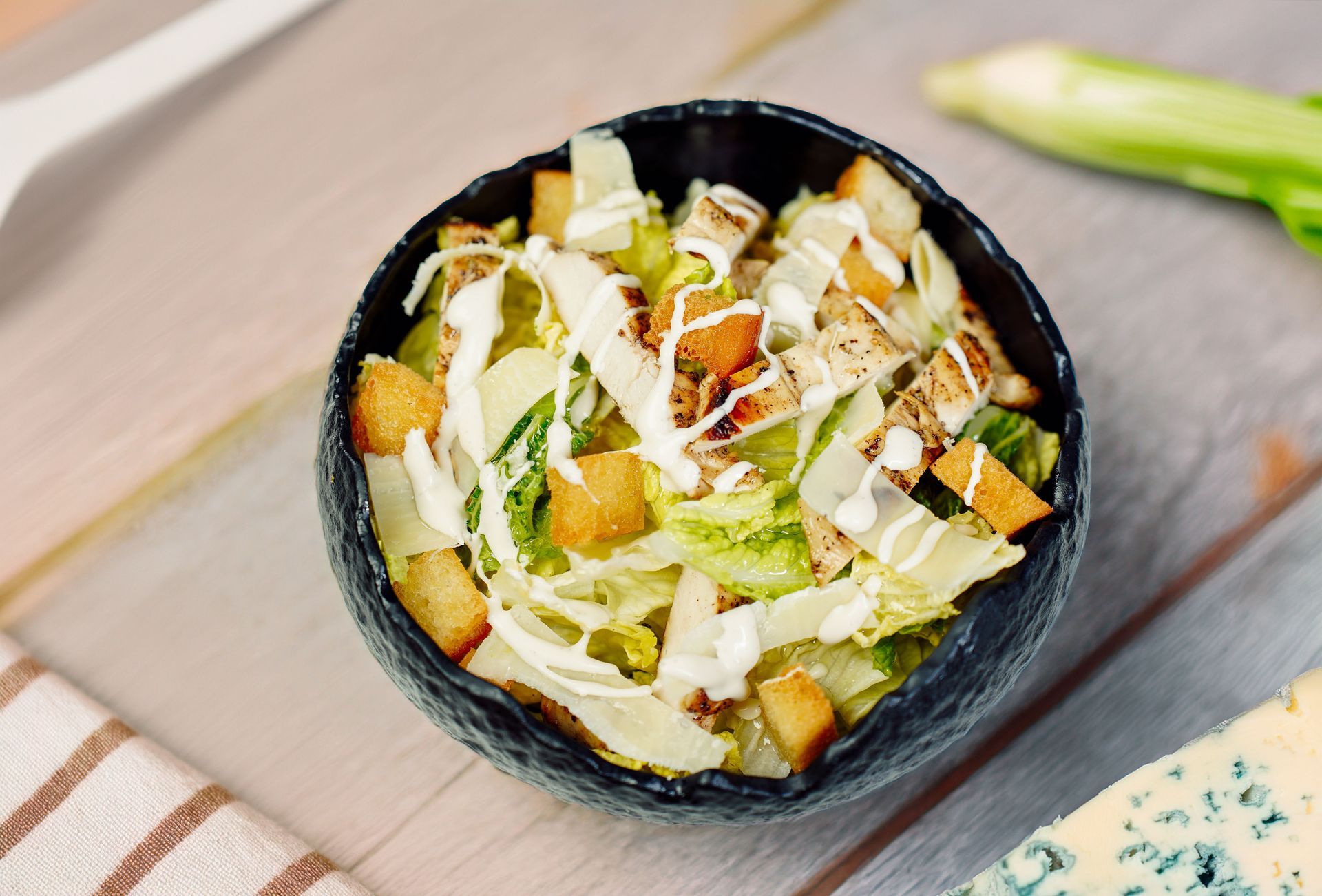 Bowl of salad with greens, croutons, and creamy dressing on a wooden table