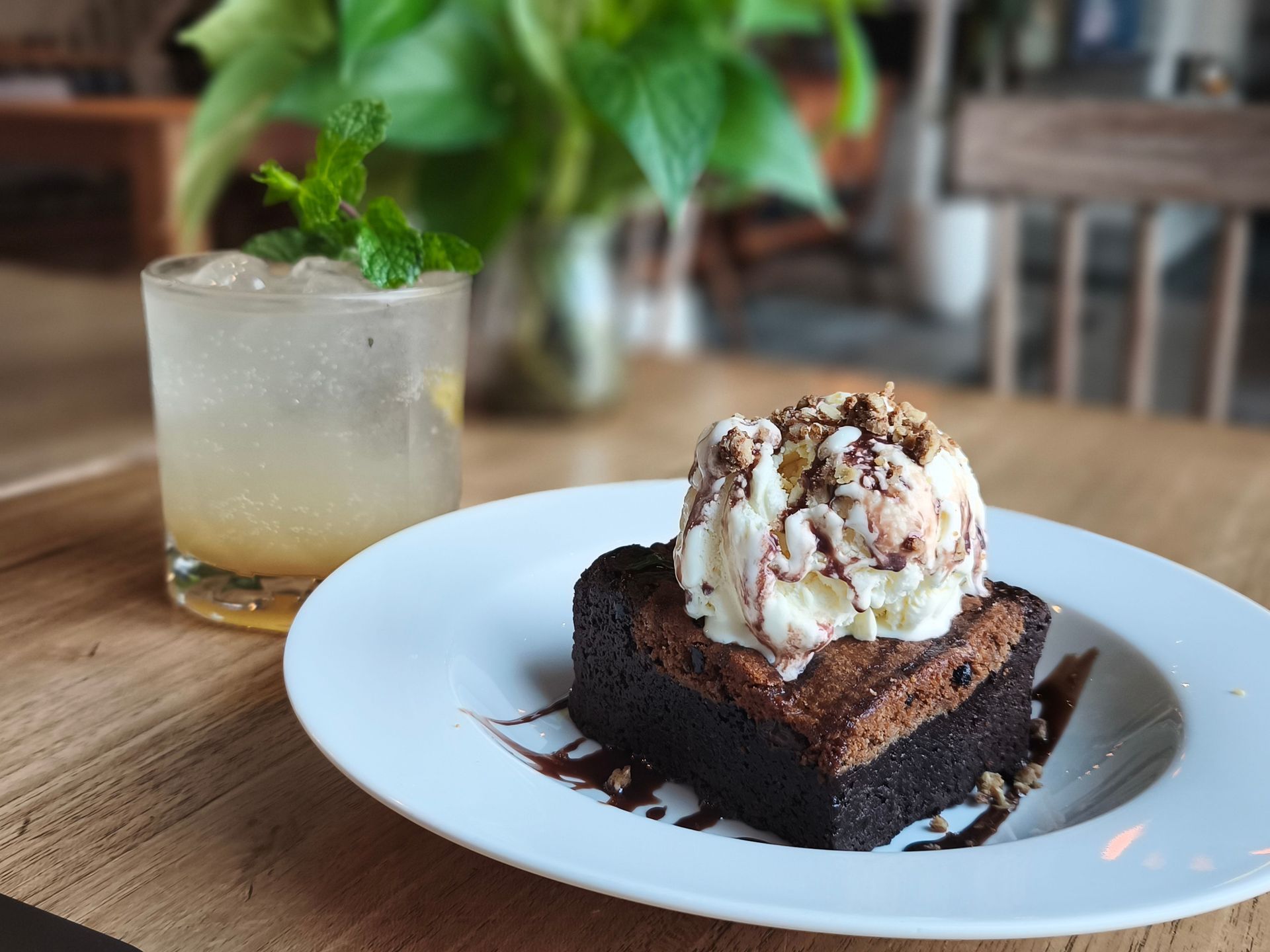 Chocolate dessert with ice cream on a white plate beside a cold drink on a wooden table