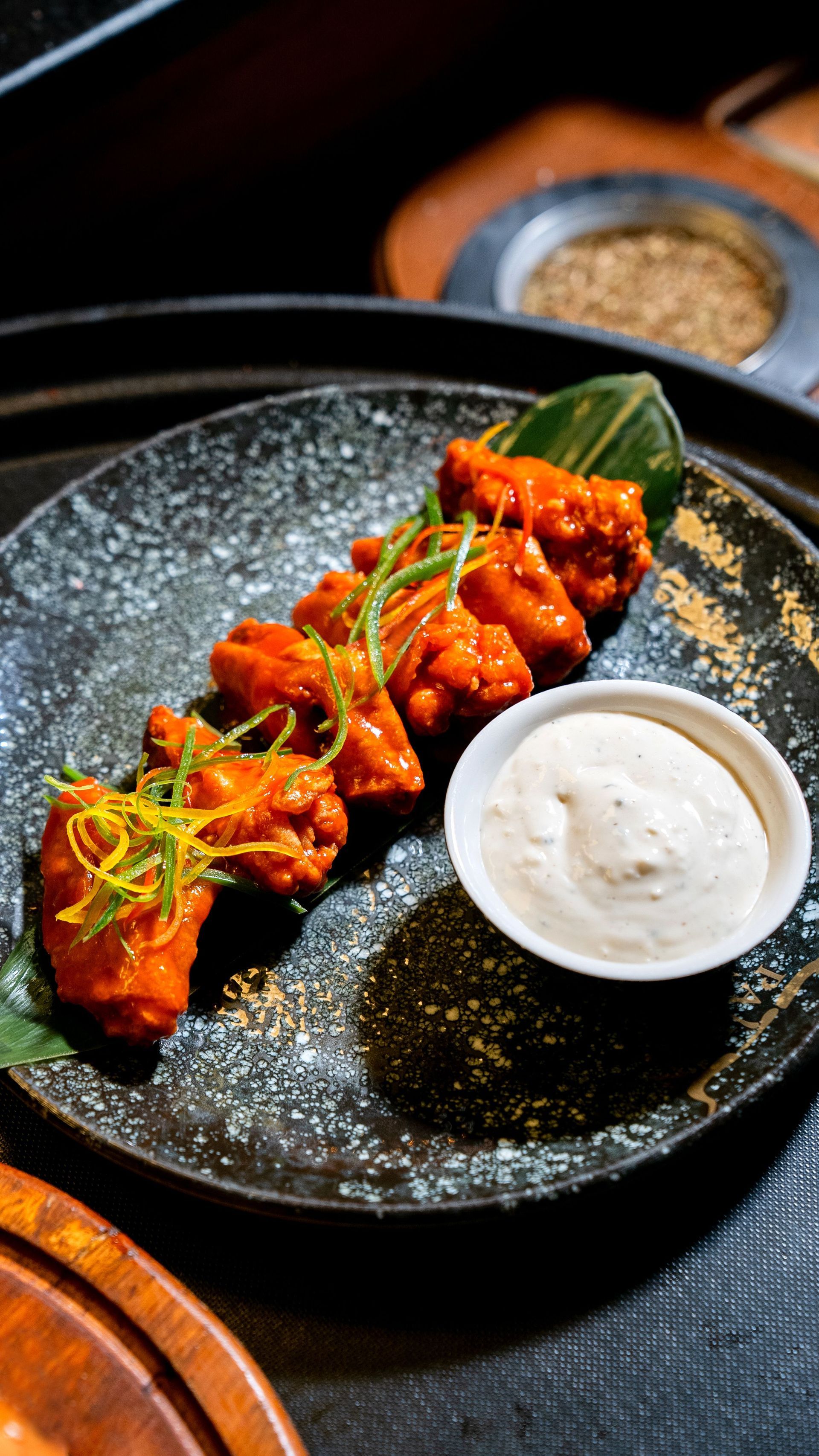 Spicy glazed skewers on a black plate with a white dipping sauce, garnished with herbs