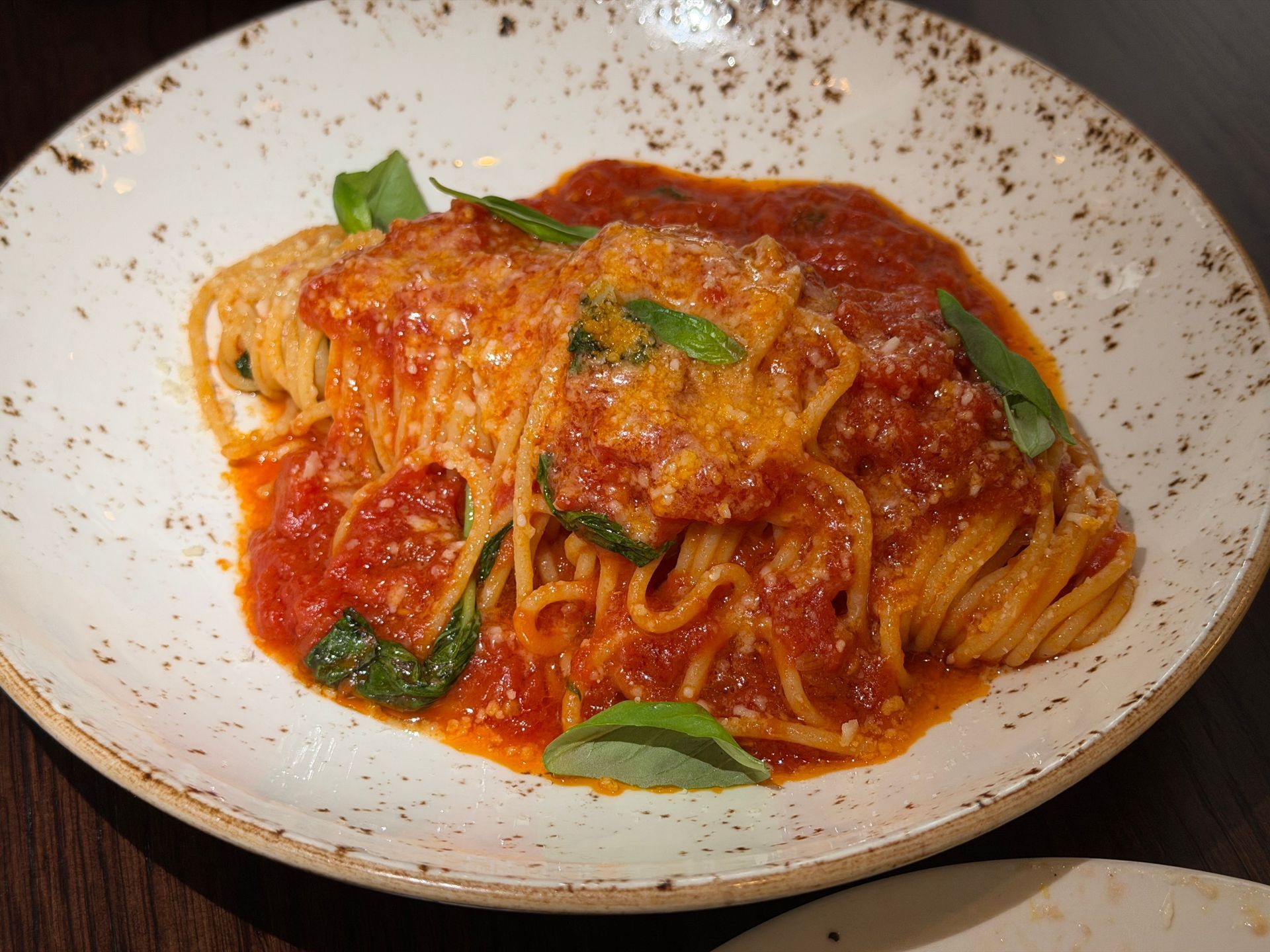 Plated pasta in red tomato sauce with basil leaves on a white speckled dish