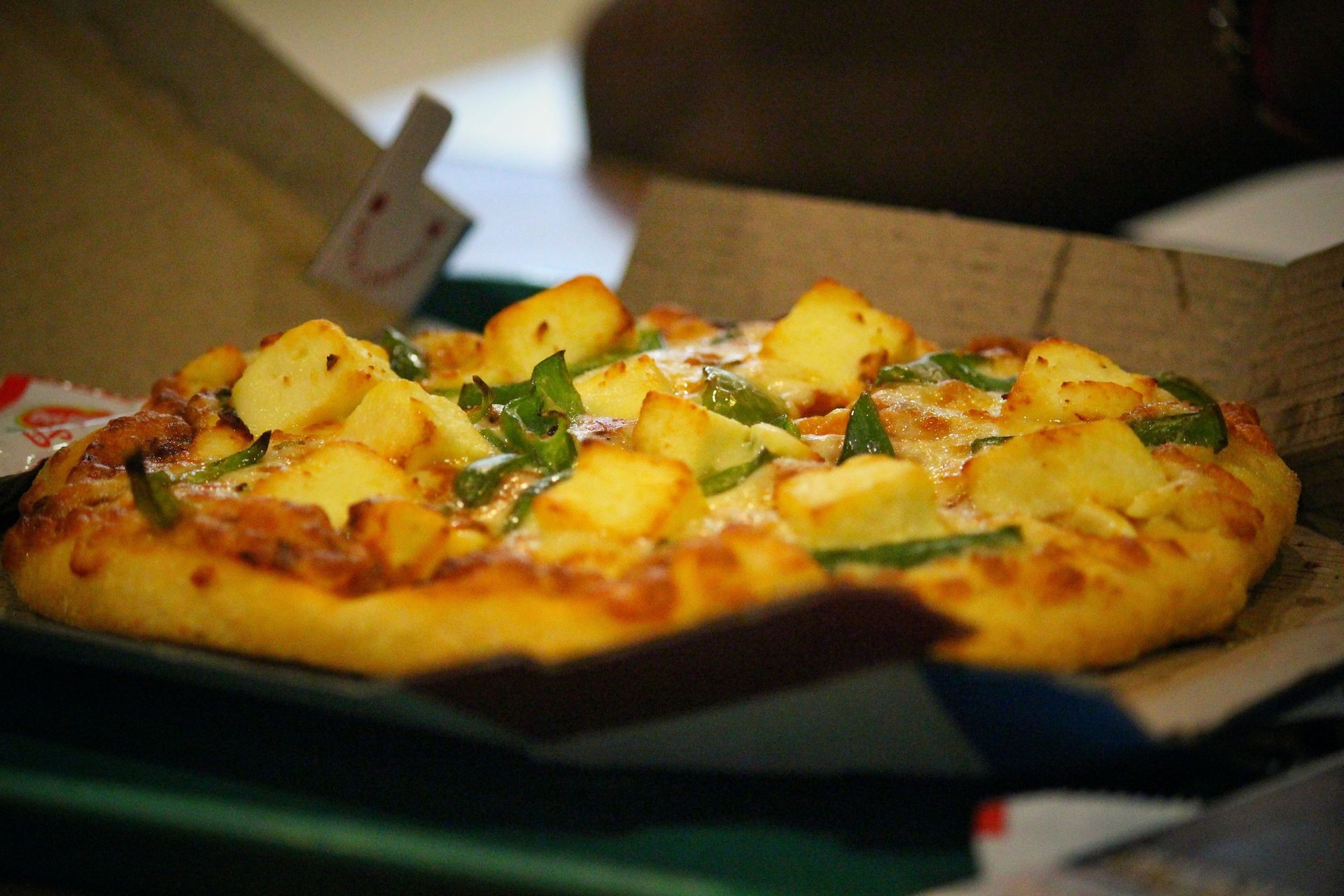 Fresh pizza with melted cheese and pineapple in a cardboard box