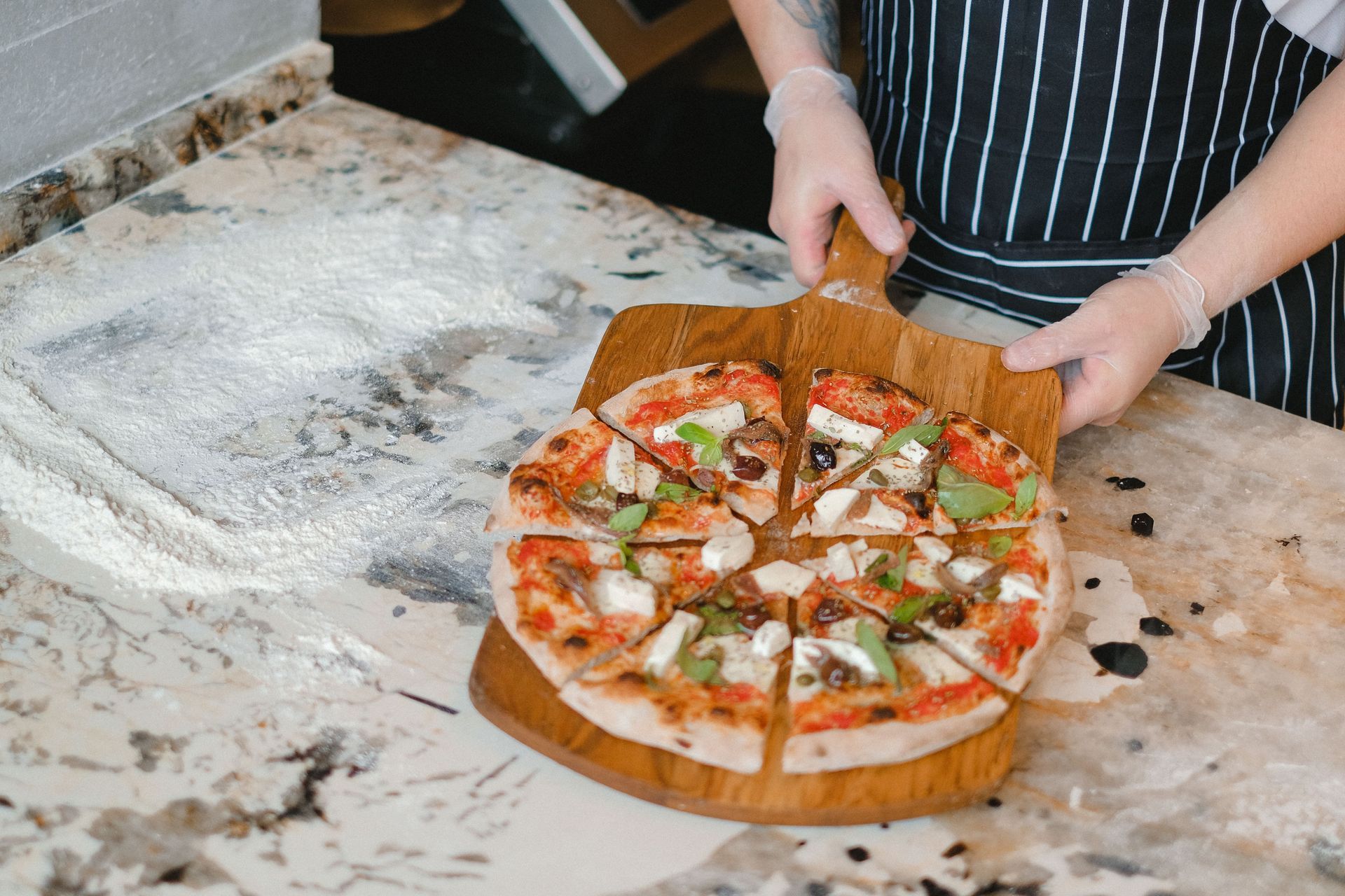 Person holding a fresh pizza on a marble countertop in a kitchen