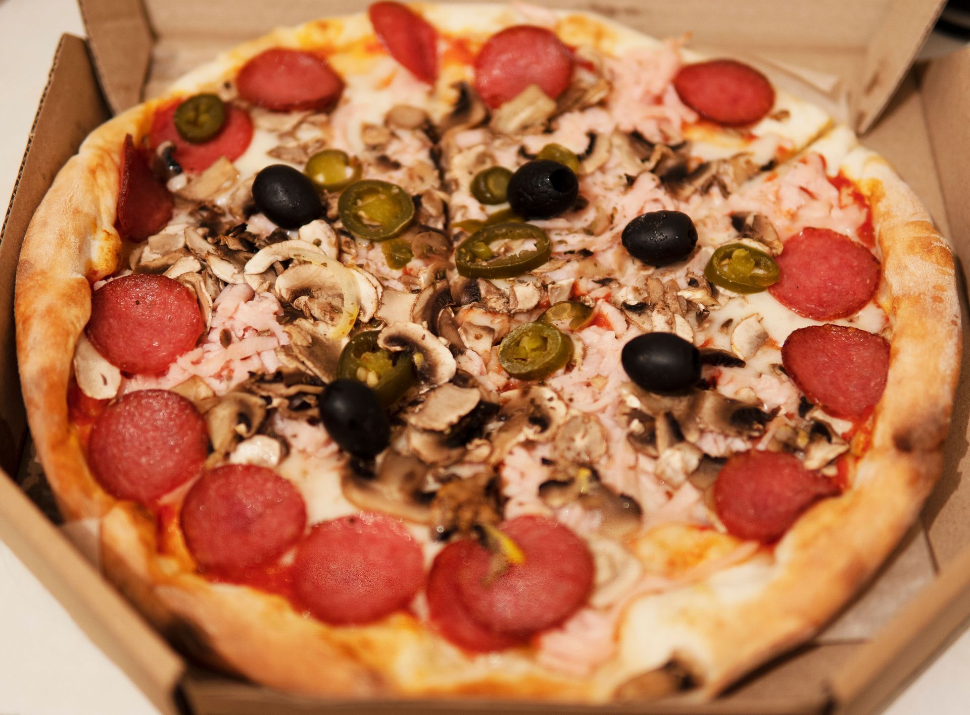 Pepperoni, mushroom, olive, and jalapeño pizza in an open cardboard box