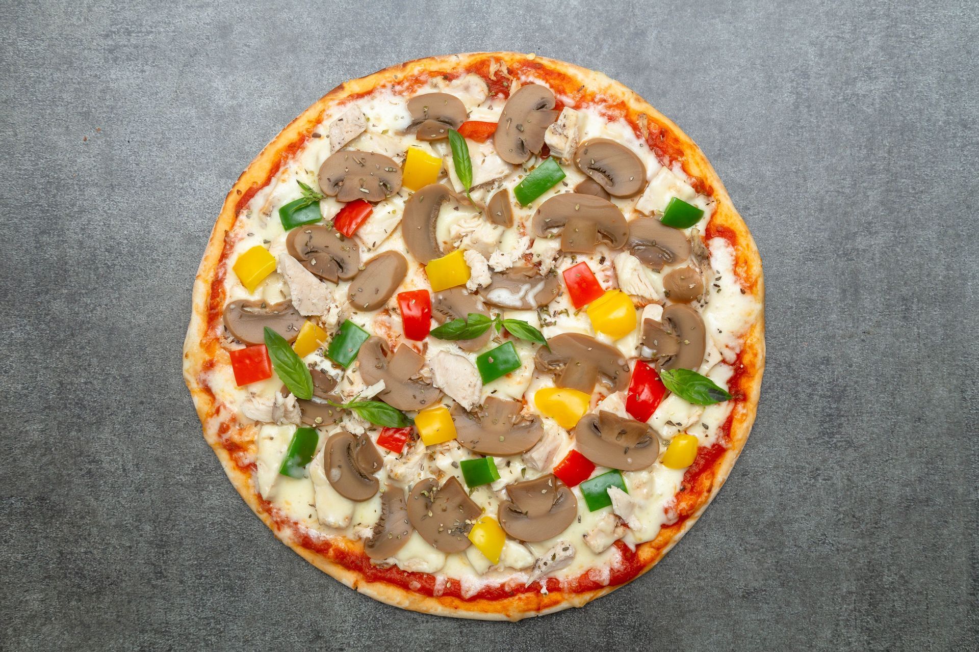 Round vegetable and mushroom pizza on a gray surface, topped with cheese, peppers, and mushrooms
