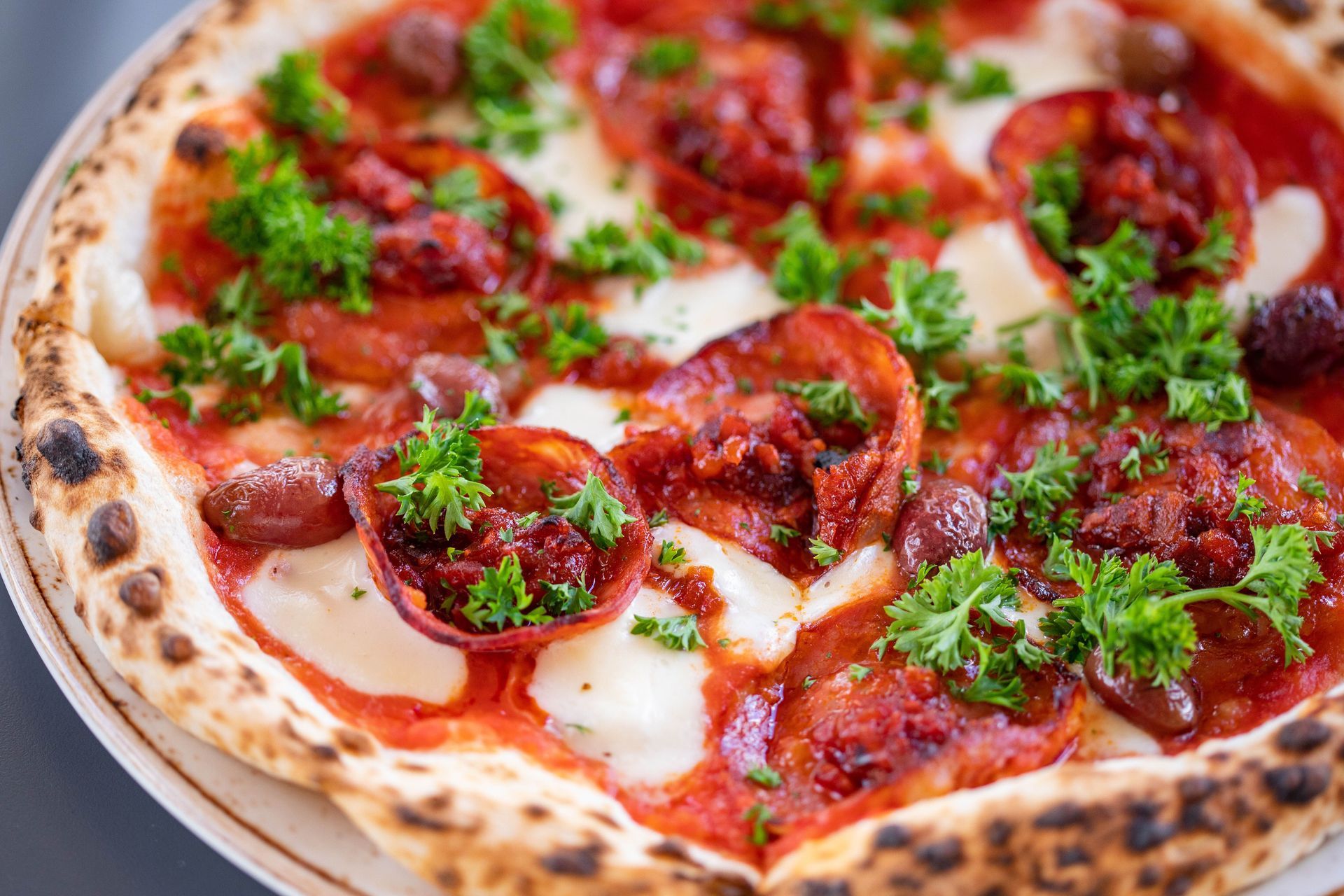 Close-up of a pepperoni pizza with melted cheese, tomato sauce, and chopped herbs on a wooden board