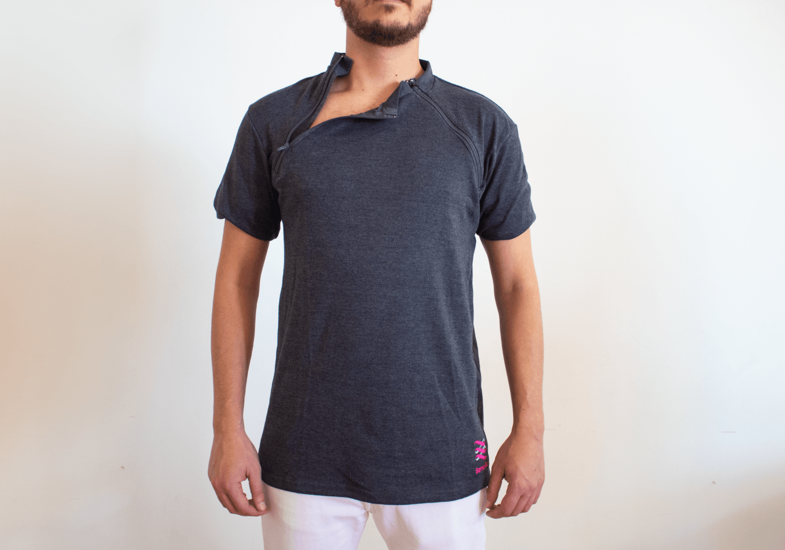 A man with a beard is wearing a gray t-shirt with a zipper on the front.