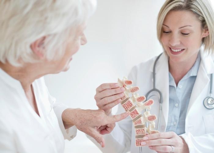 Un médico le muestra un modelo de columna vertebral a un paciente en un consultorio médico bien iluminado.