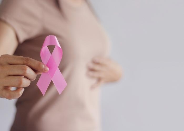 Mano sosteniendo una cinta rosa de concienciación sobre el cáncer de mama frente al torso de una persona.