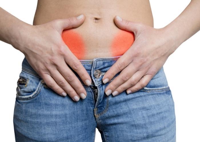 Manos en la parte baja de la espalda con la zona del dolor resaltada en rojo por encima de la cintura de los pantalones vaqueros.