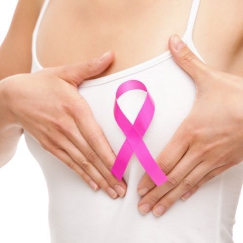 Manos sosteniendo un lazo rosa de concienciación sobre el cáncer de mama sobre el pecho de una mujer.