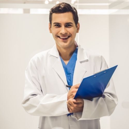 oncology Un médico sonriente con bata blanca sosteniendo un portapapeles azul en el luminoso pasillo de una clínica.