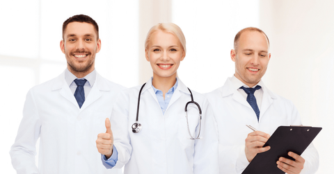 Medicamento Capecitabina Tres profesionales médicos con batas blancas, sonriendo, uno de ellos sosteniendo un portapapeles y el otro levantando el pulgar.