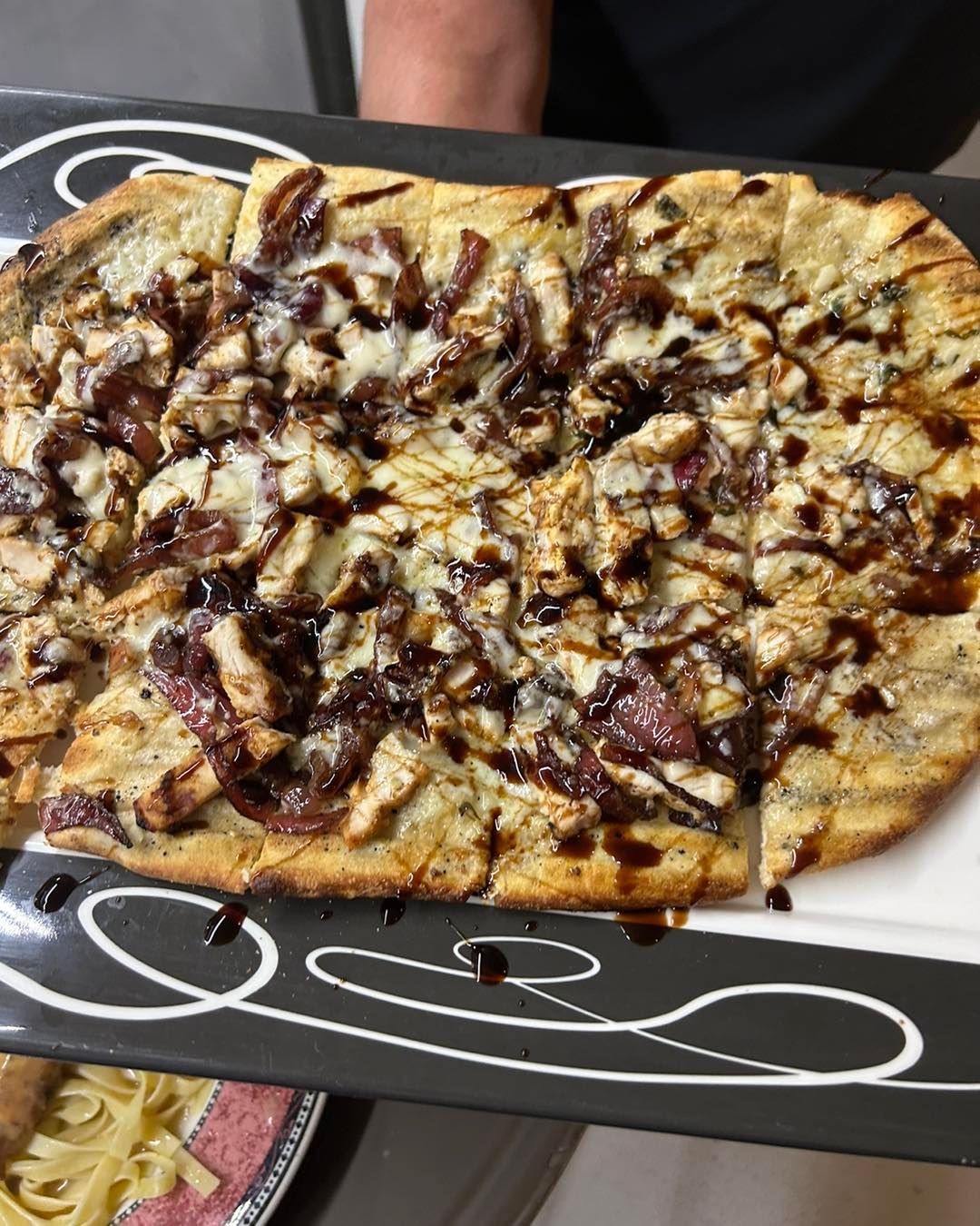 A person is holding a white plate with a pizza on it.