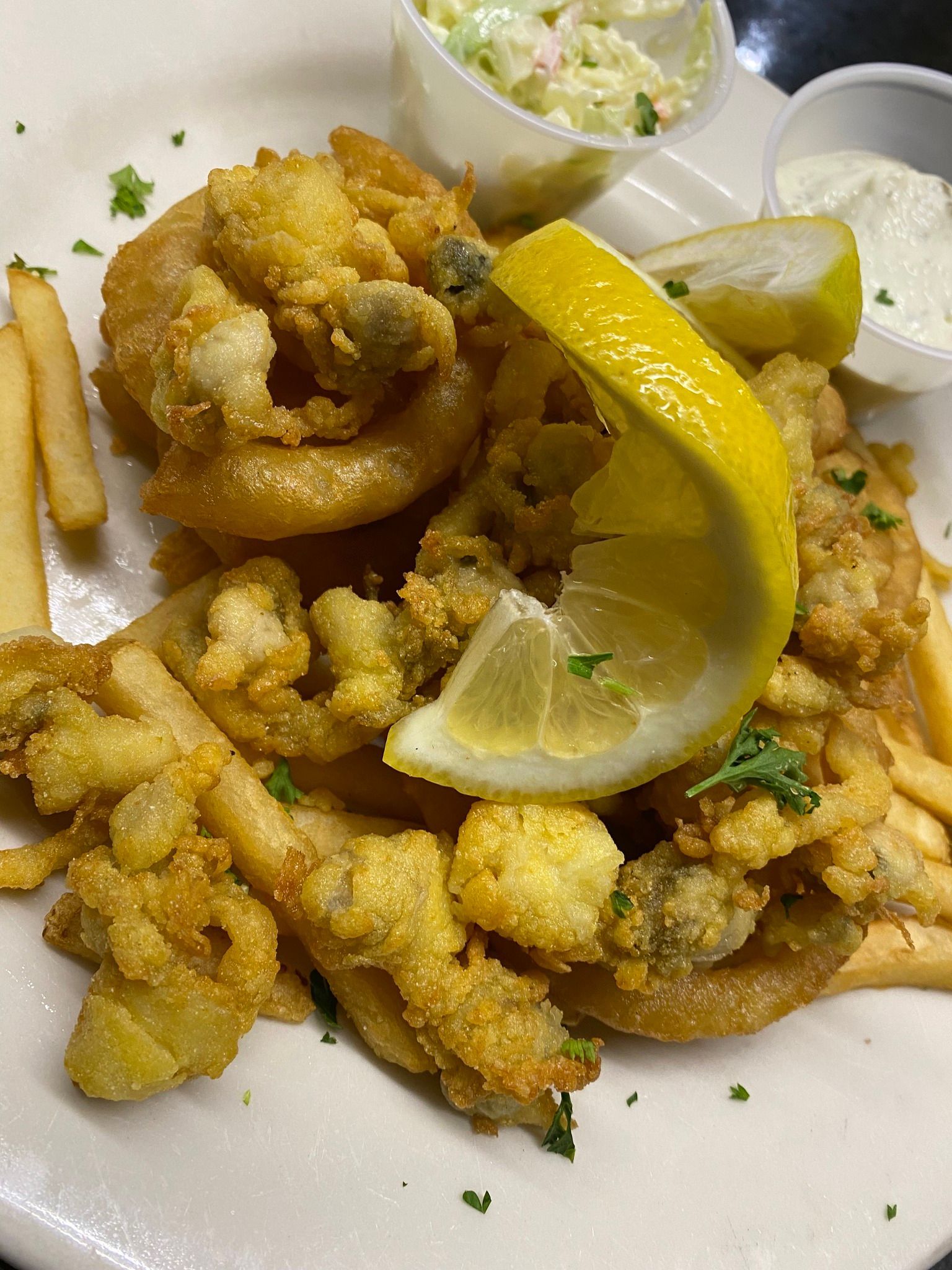 A plate of fried seafood with french fries and coleslaw on a table.