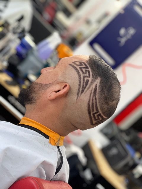 Barber trimming a client&rsquo;s dark hair in a salon, with a fade haircut in progress