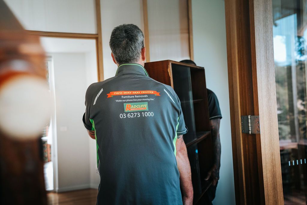 Person in teal shirt stands in a doorway, facing away in a room with wooden trim and a mirror.