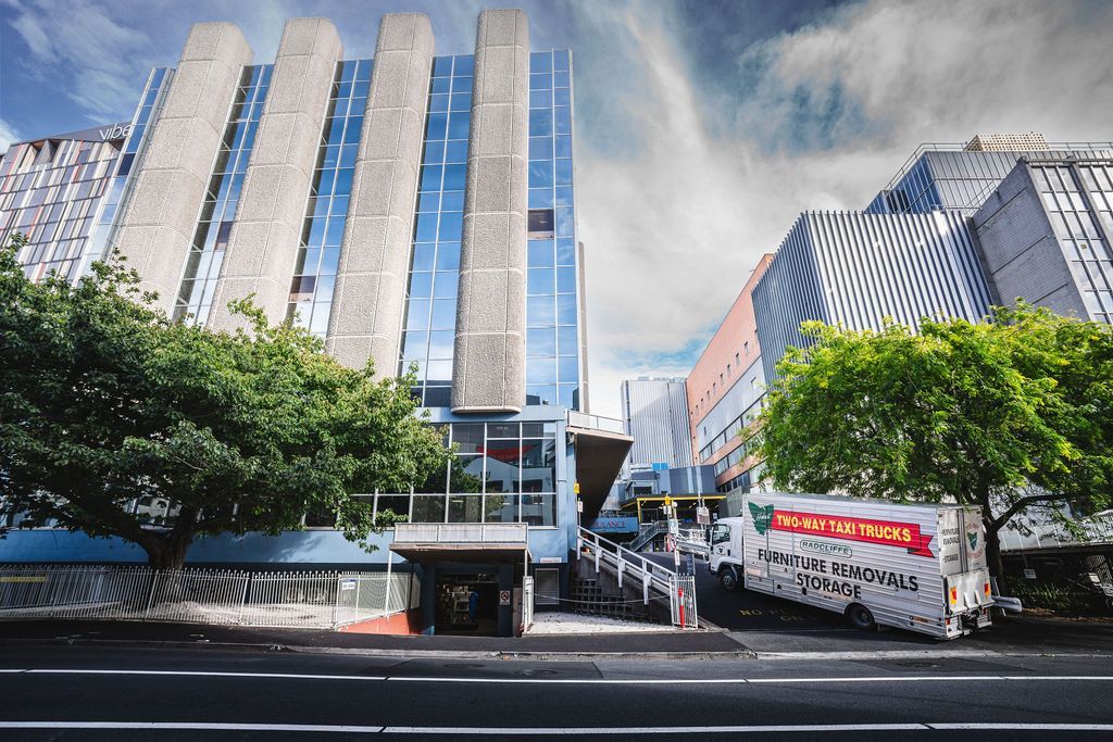 Modern city street with tall office buildings, trees, and a truck passing by