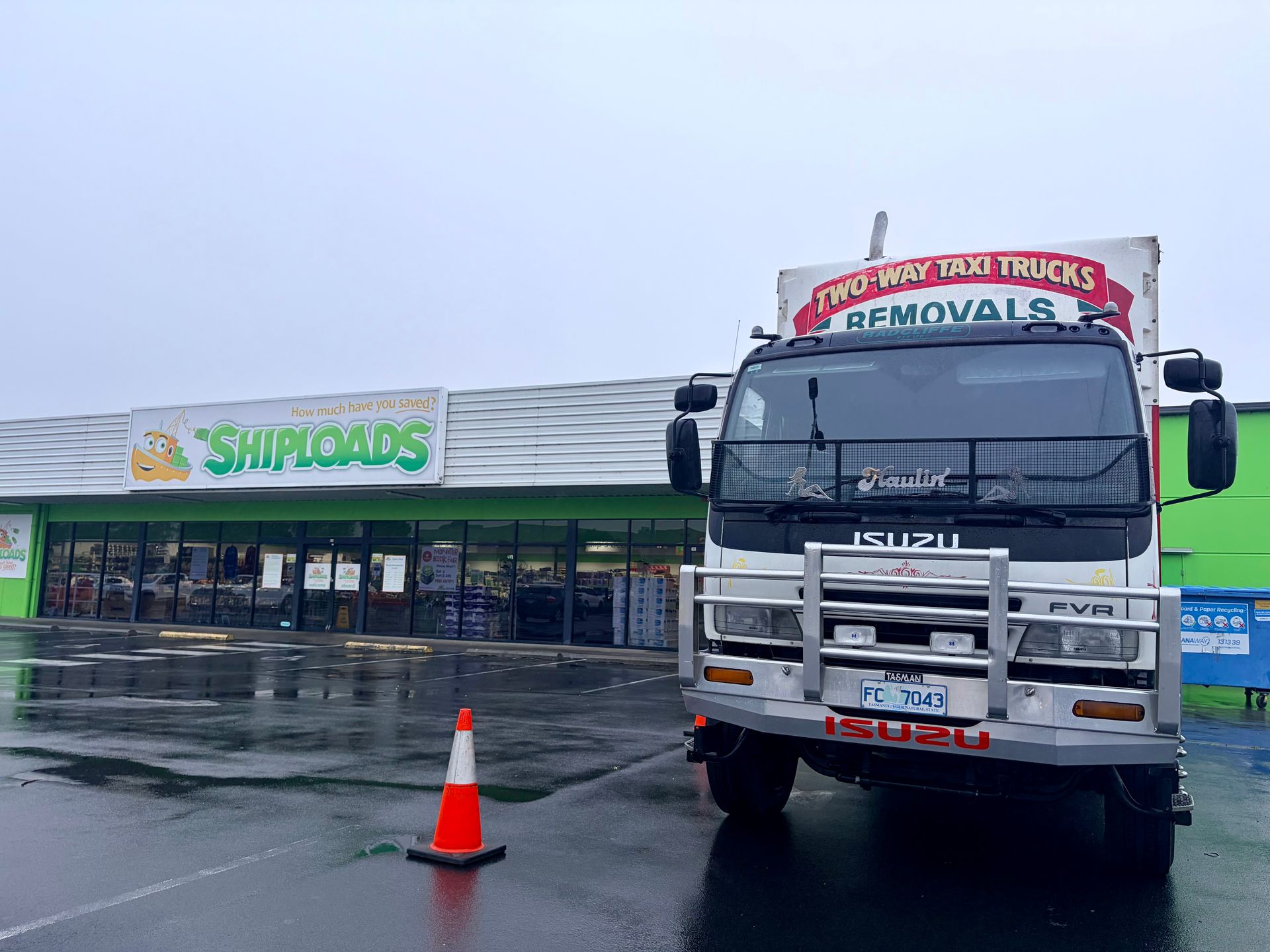 Tow truck parked in front of a Smith's store on a rainy day, with an orange cone in the foreground