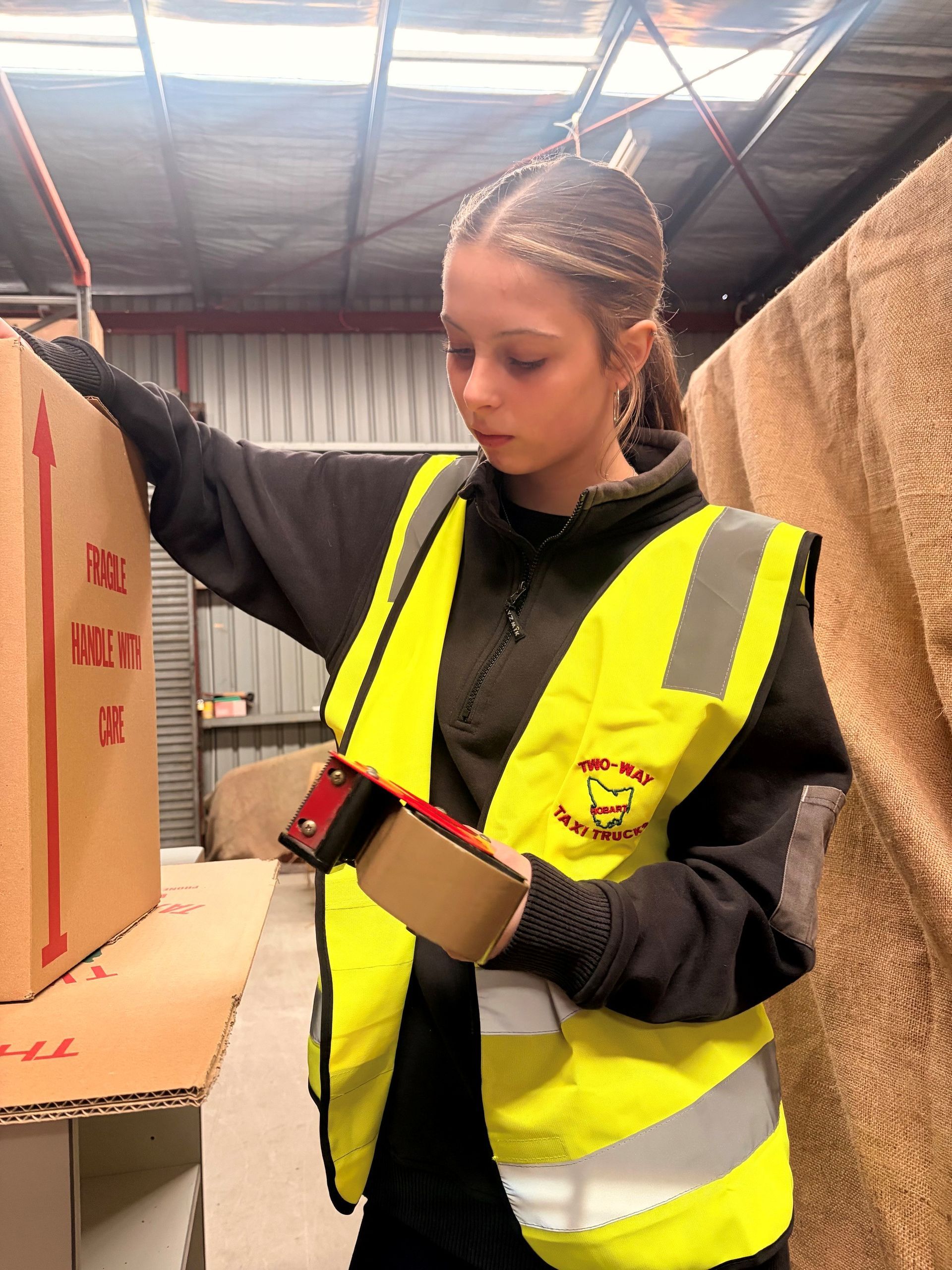 Person in a yellow safety vest writing on a clipboard in a warehouse aisle.