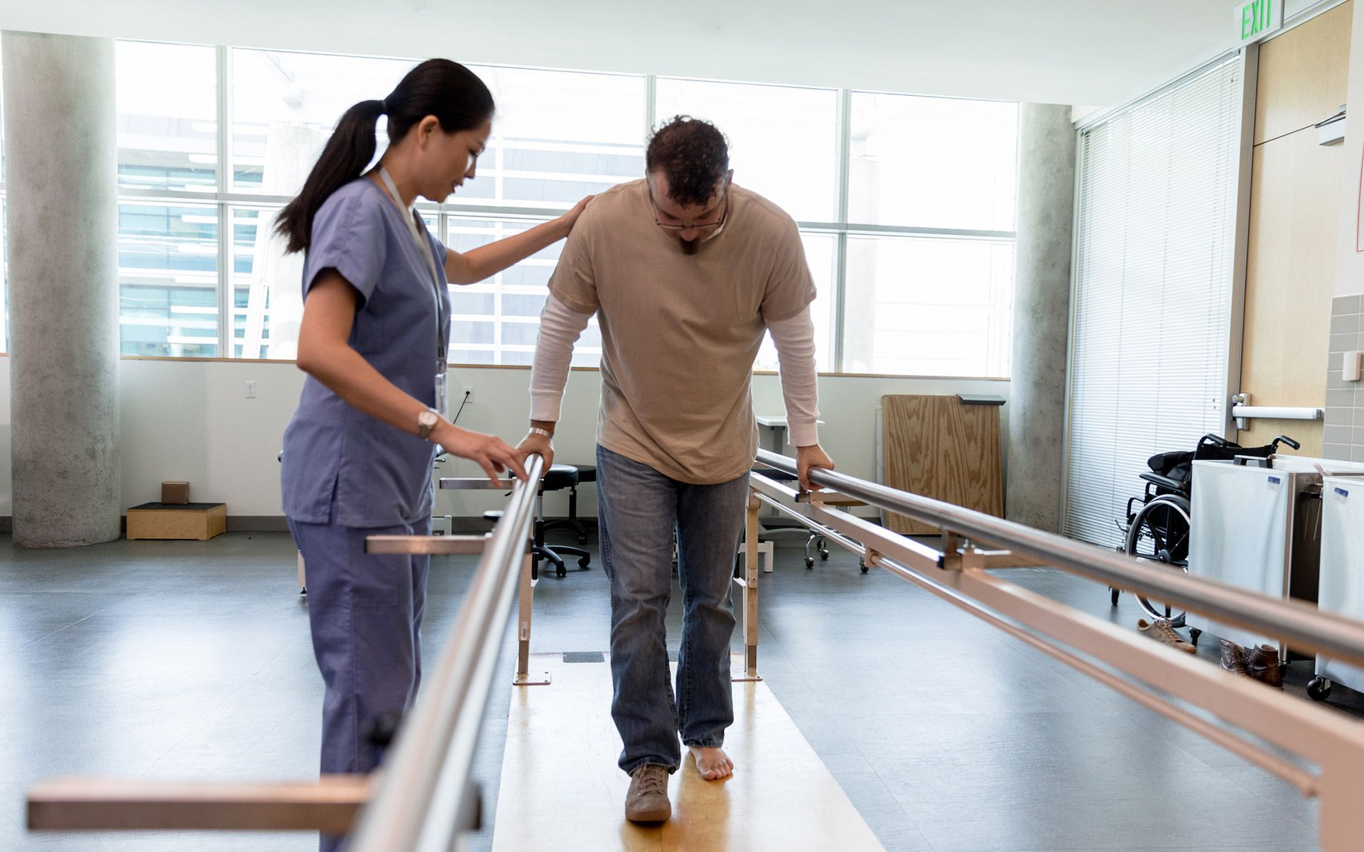 Physical therapist helping a man walk on parallel bars in a rehab clinic