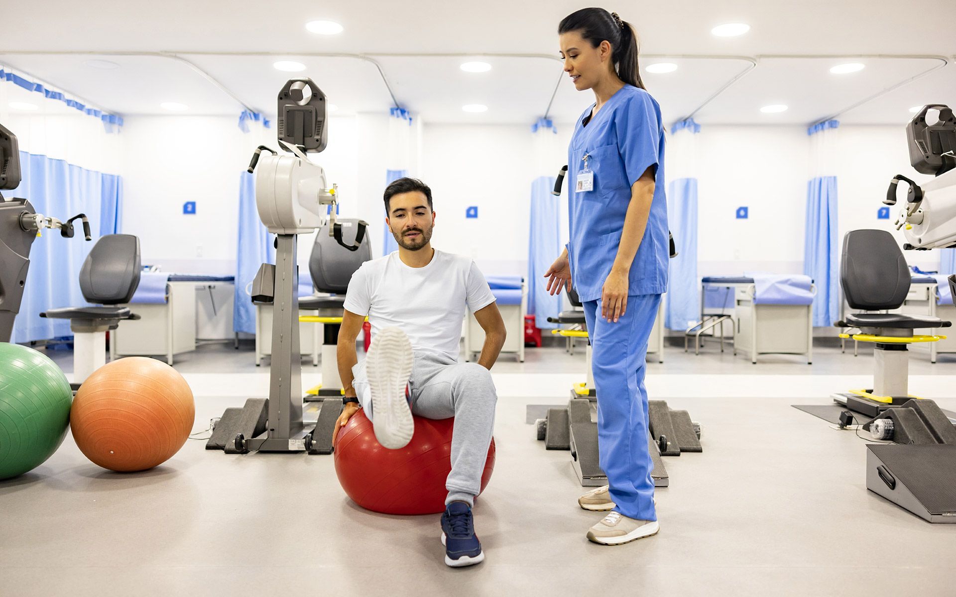 Therapist assisting patient with exercise ball in a bright rehabilitation gym with fitness equipment