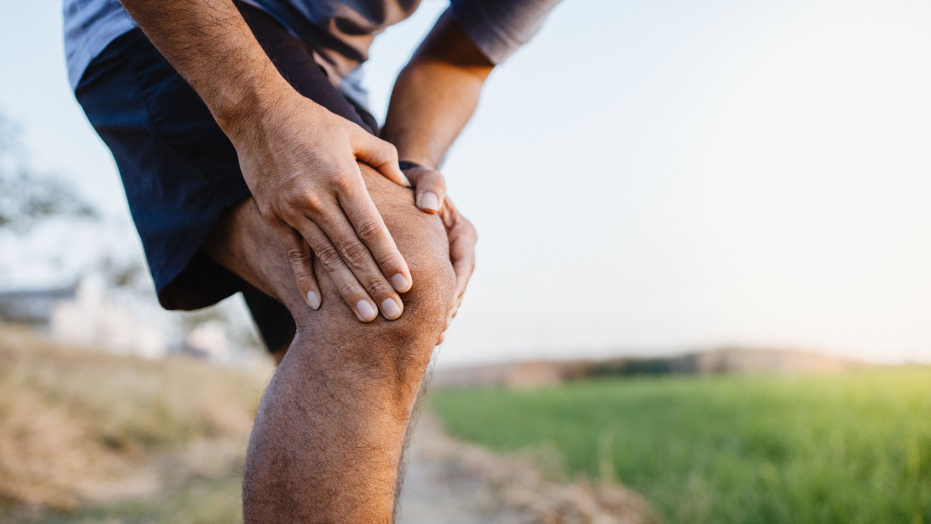 Person holding a bent knee outdoors, suggesting knee pain during exercise or a walk