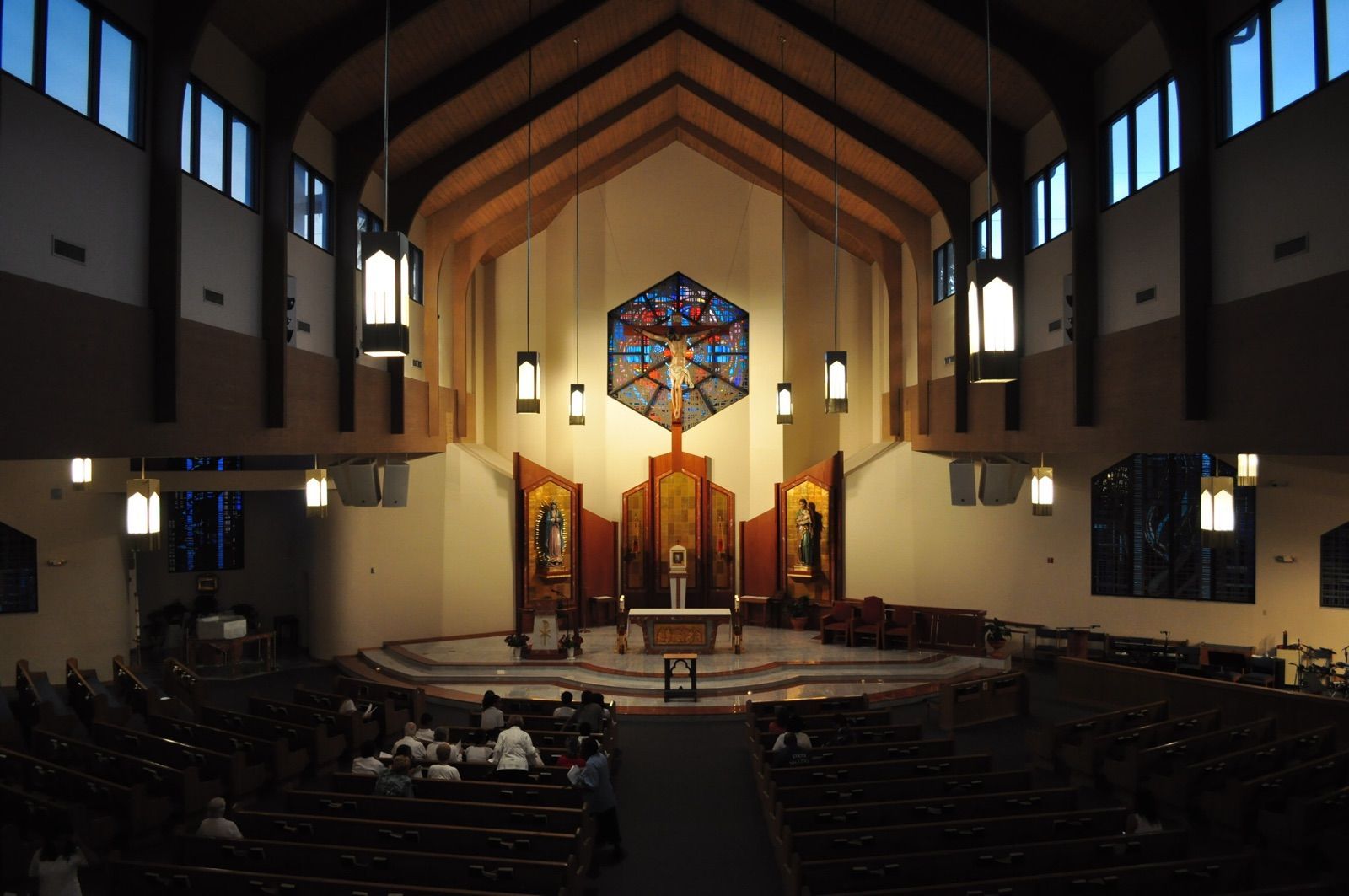 Church sanctuary interior with pews, altar, and stained-glass window under vaulted wooden ceiling