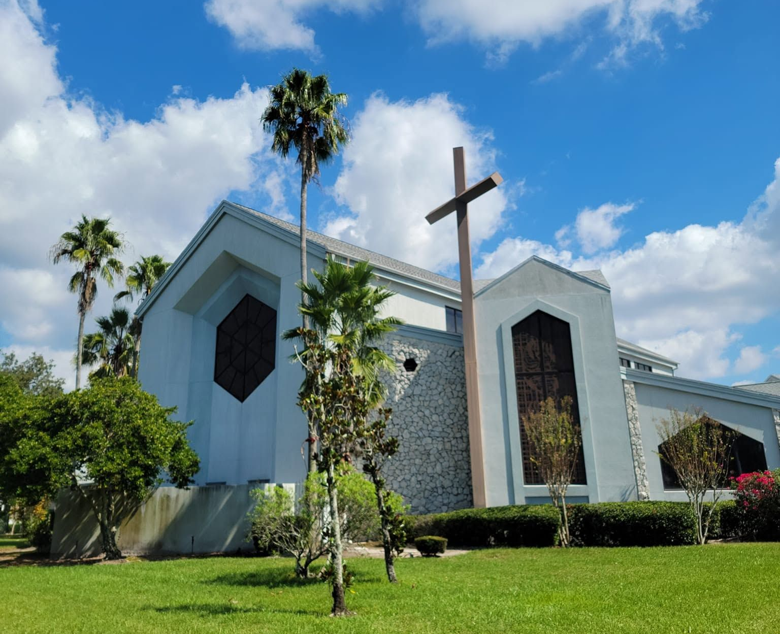 White church with a large cross and tall windows on a sunny green lawn under a blue sky